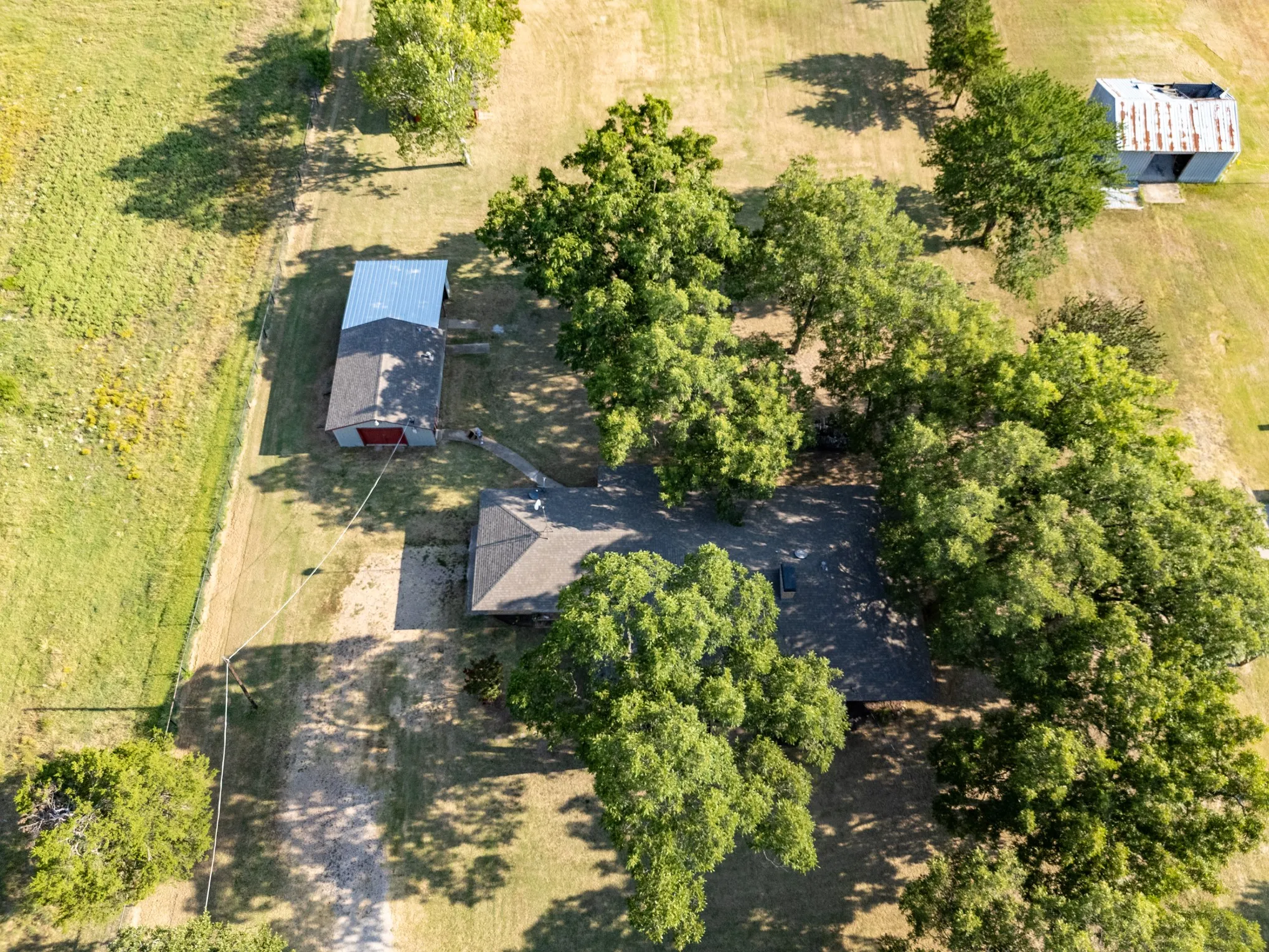 Expansive property featuring a main residence with a gabled roof, two detached outbuildings, and mature trees