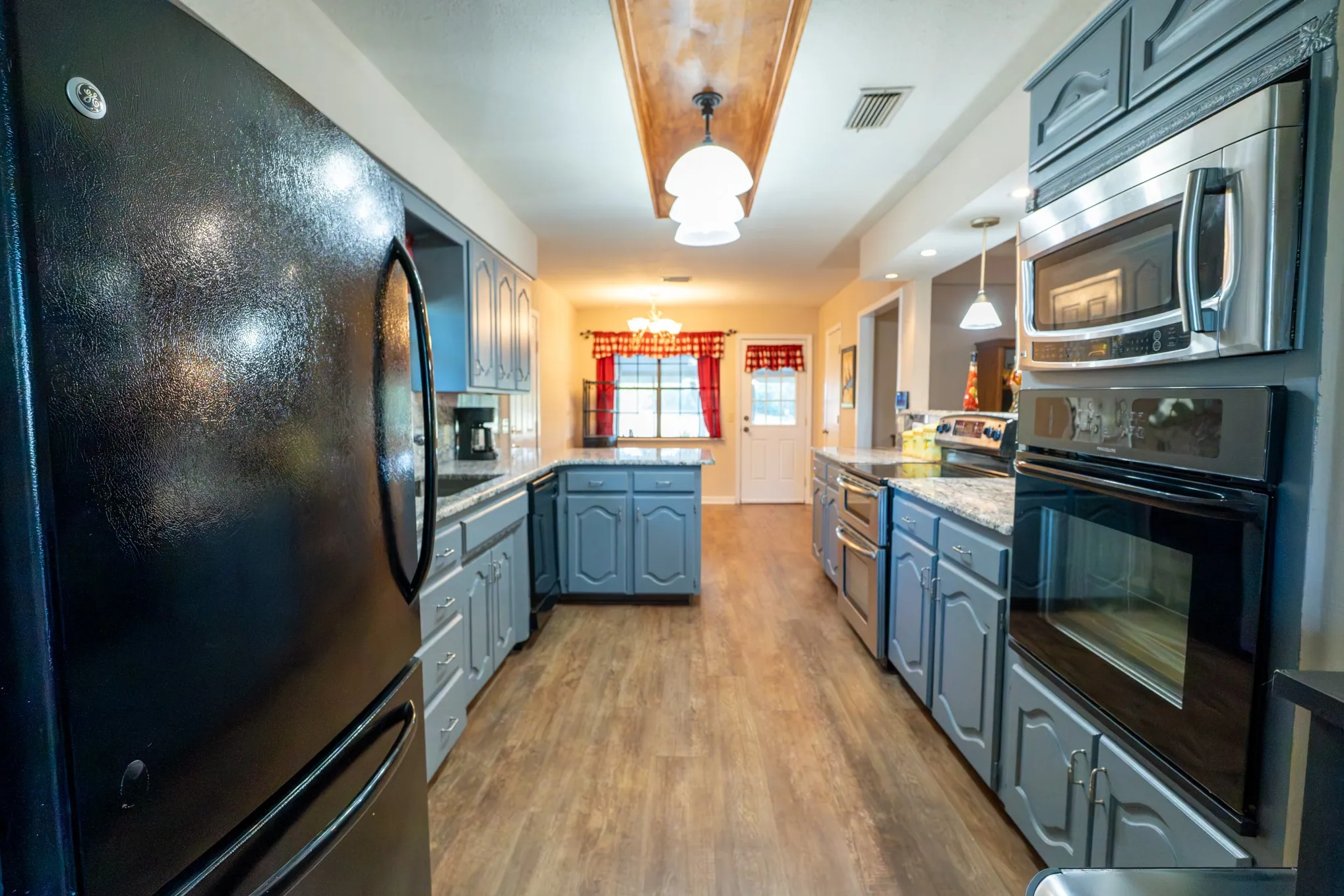 Galley kitchen featuring wood-finish flooring, two-tone cabinetry, and stainless steel appliances including a built-in oven and microwave