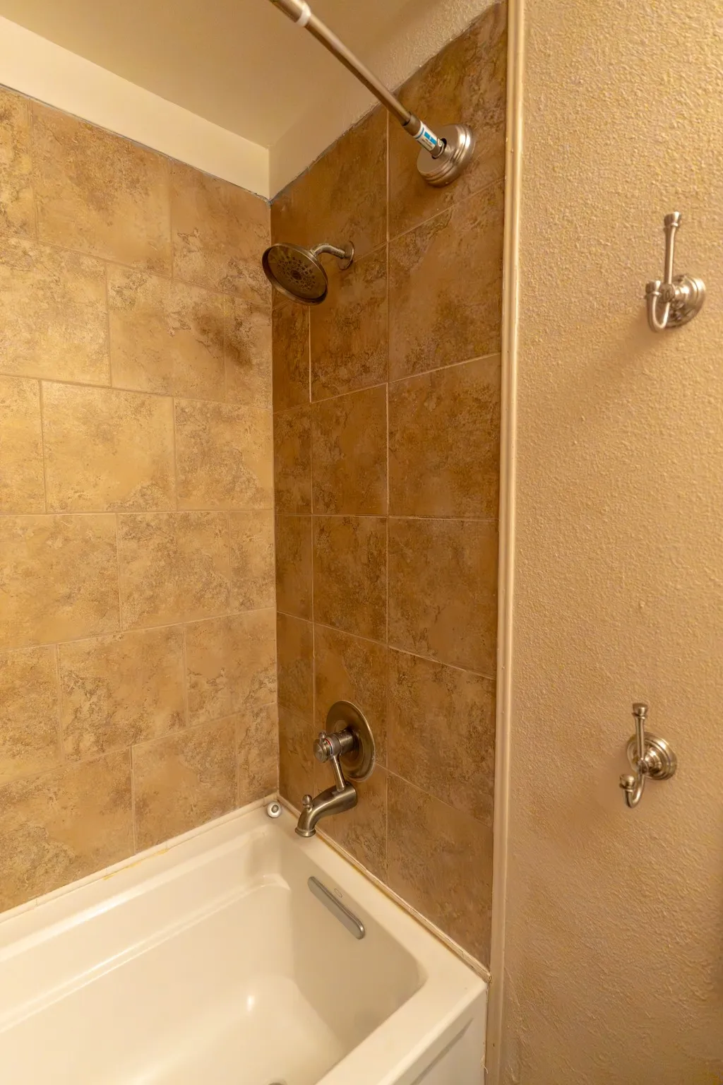 Bathtub and shower combination featuring a tiled surround, chrome showerhead, and matching chrome faucet