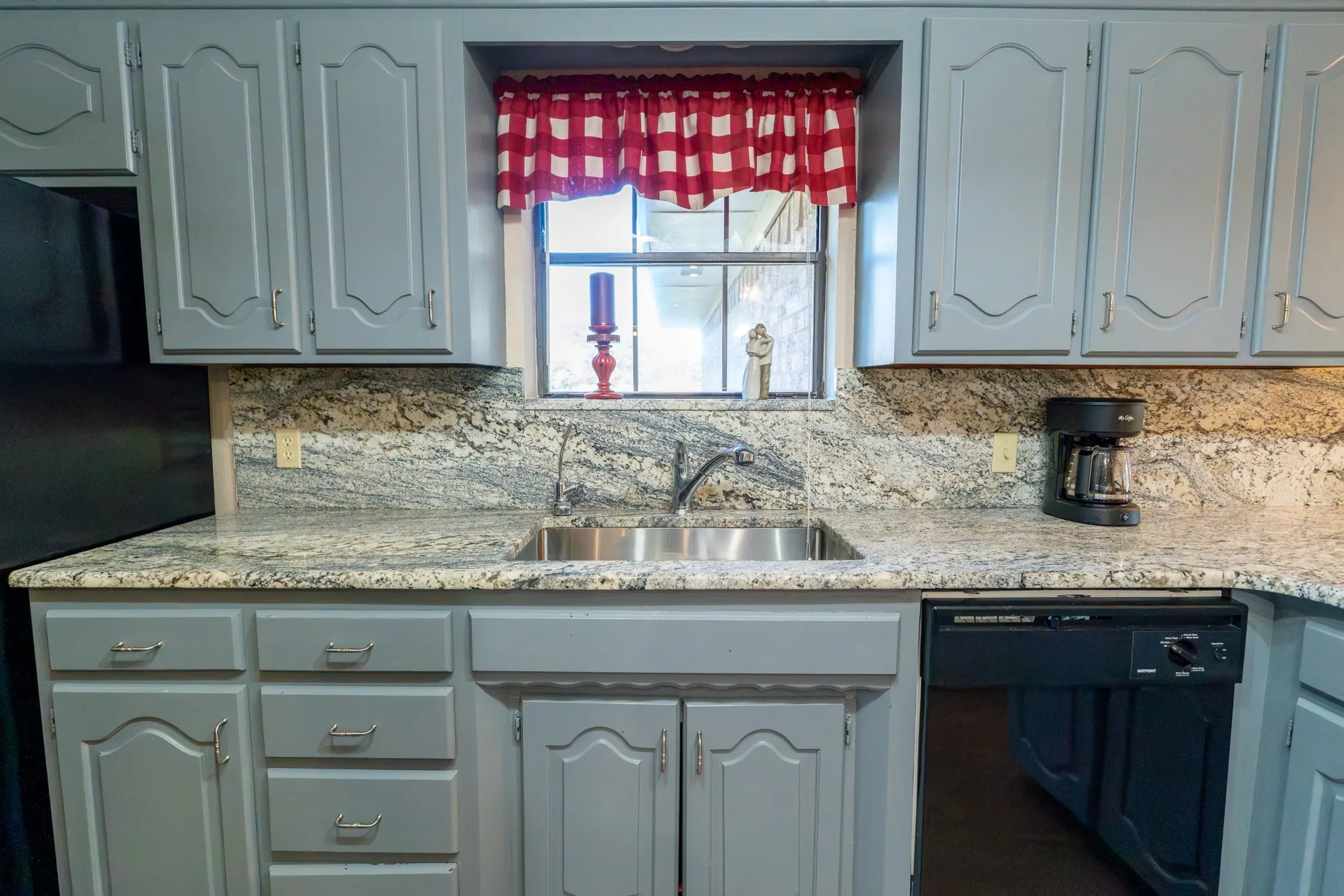 Kitchen featuring gray cabinetry, stainless steel sink, black dishwasher, and stone countertops
