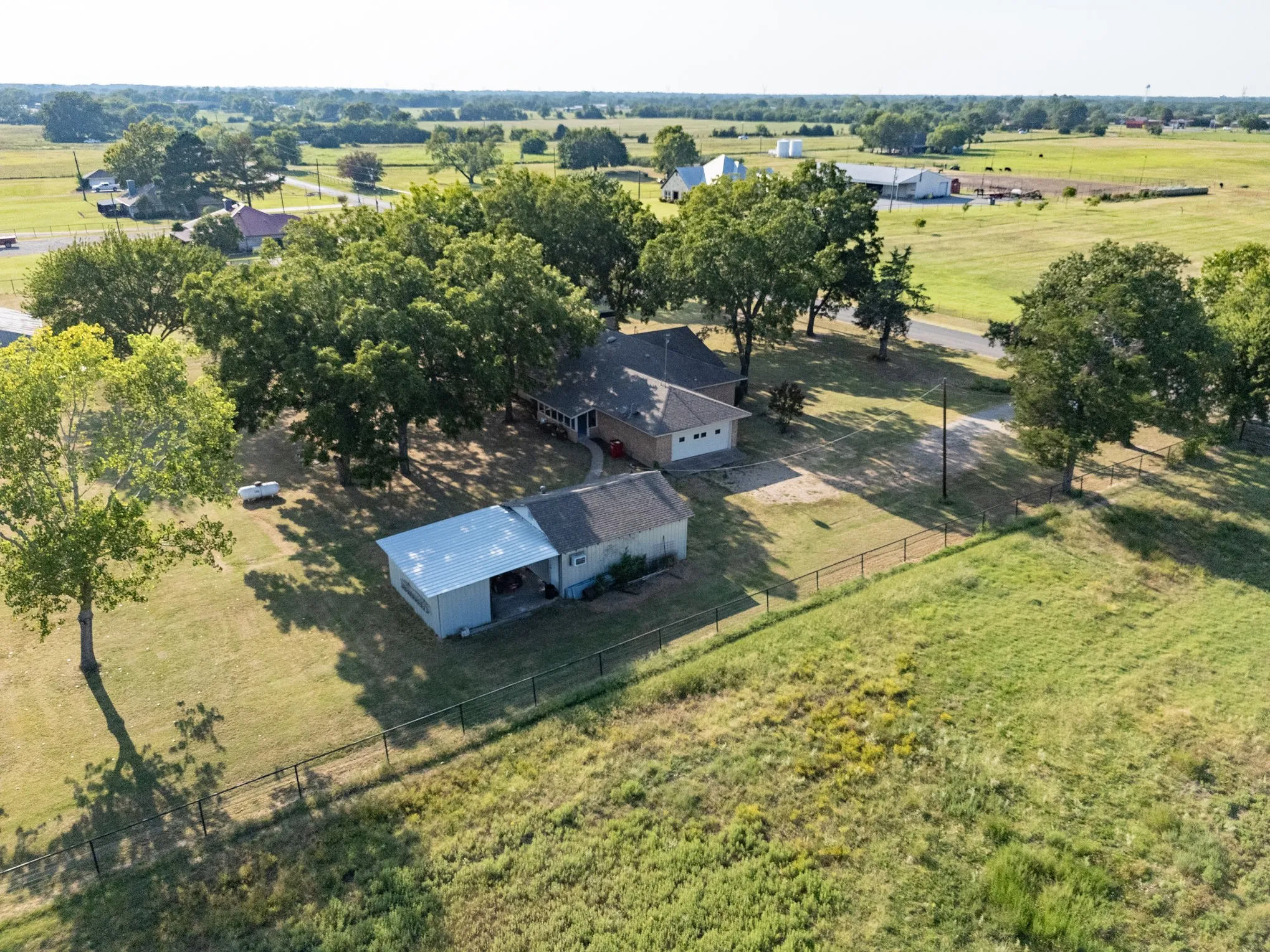 Expansive lot featuring mature trees, a detached storage building with an open-air extension, and a fenced perimeter