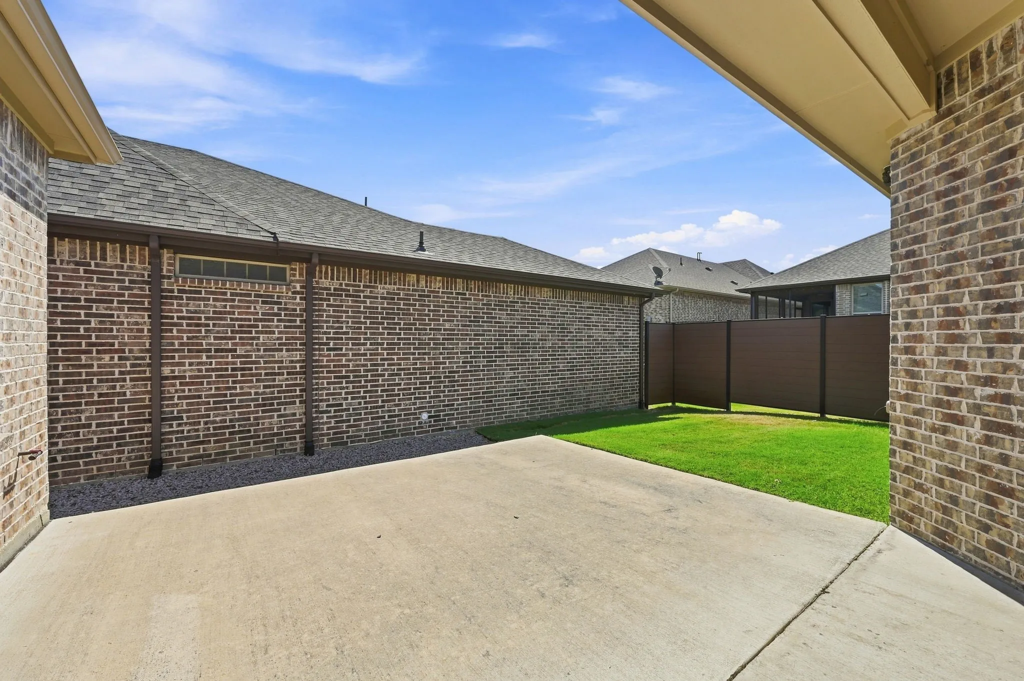Concrete patio with a manicured lawn, brick exterior, composite fencing, and a shingled roof
