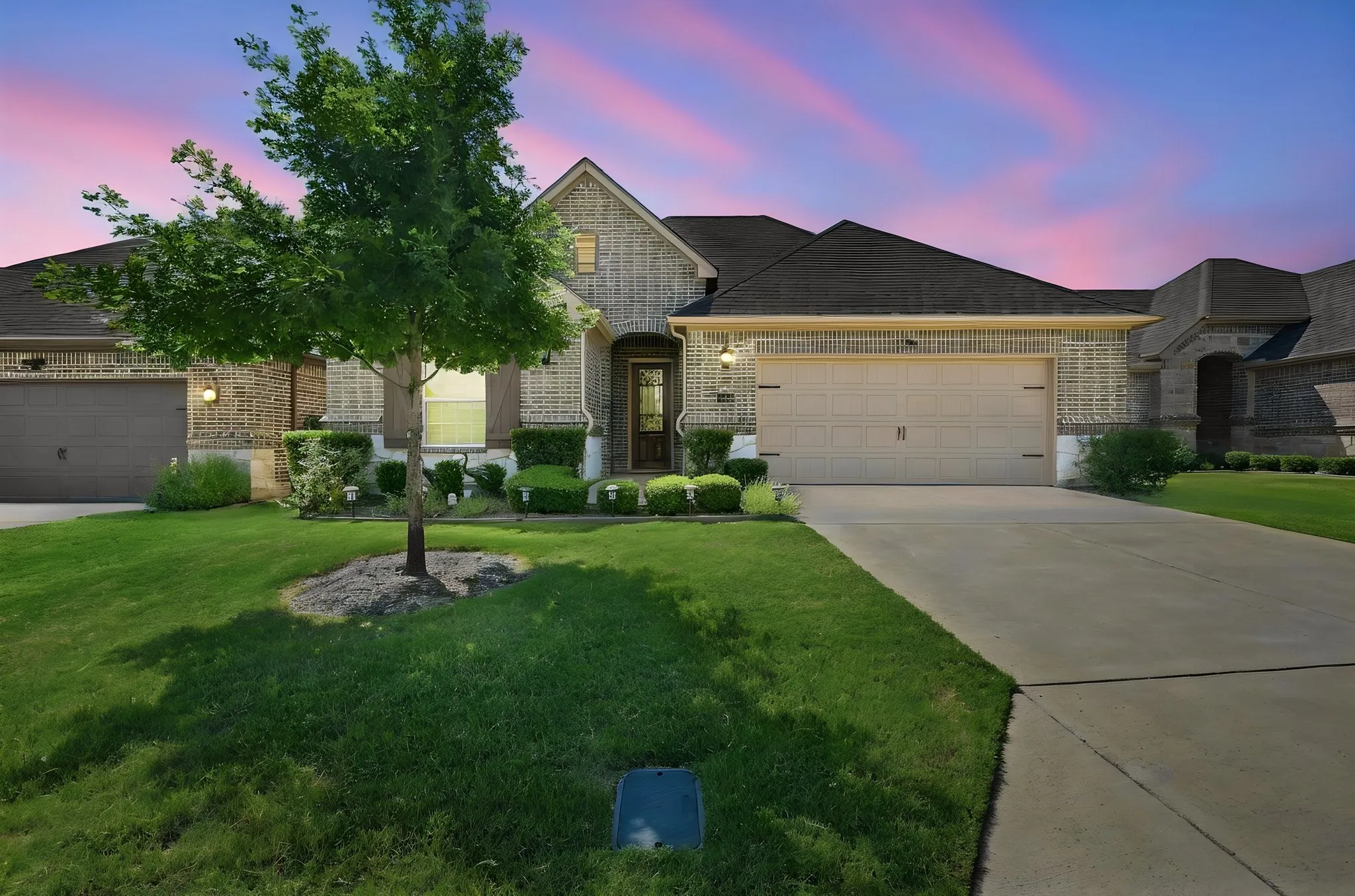 Brick facade, multiple gables, attached two-car garage, concrete driveway, and front landscaping