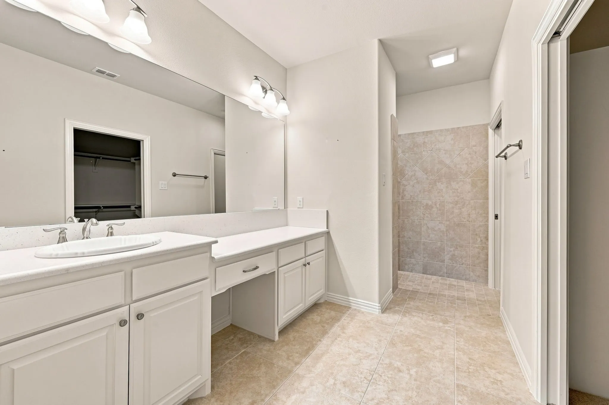 Dual vanity with white cabinetry and integrated sinks, a walk-in tiled shower, and large wall-mounted mirror
