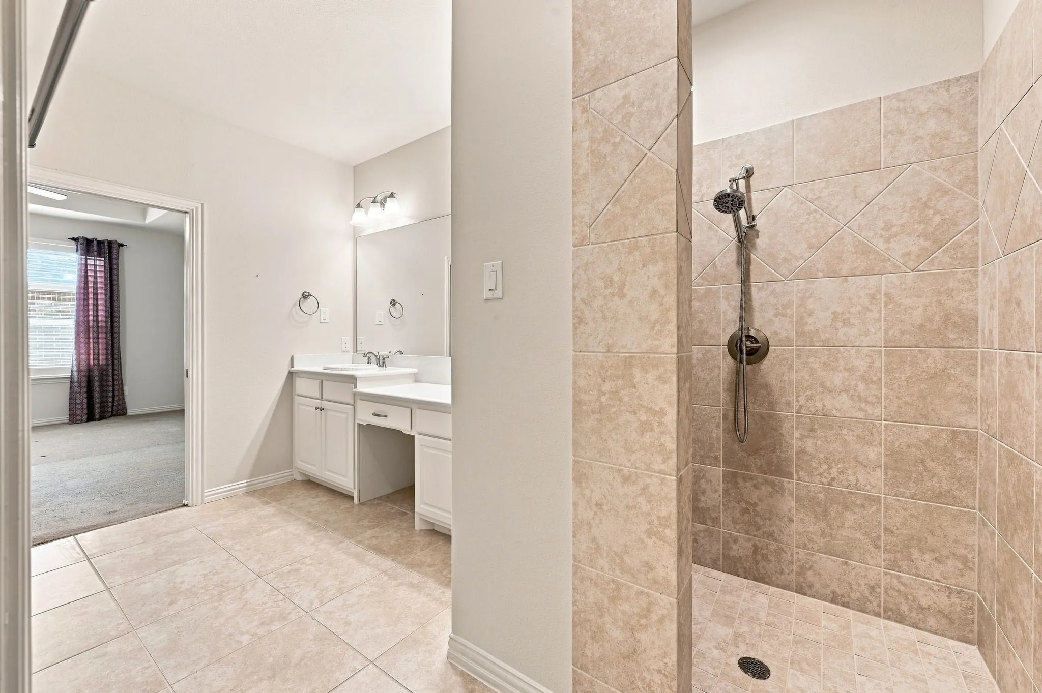 Spacious bathroom with tiled flooring, a vanity featuring dual sinks, dedicated makeup area, and a walk-in shower with tiled walls