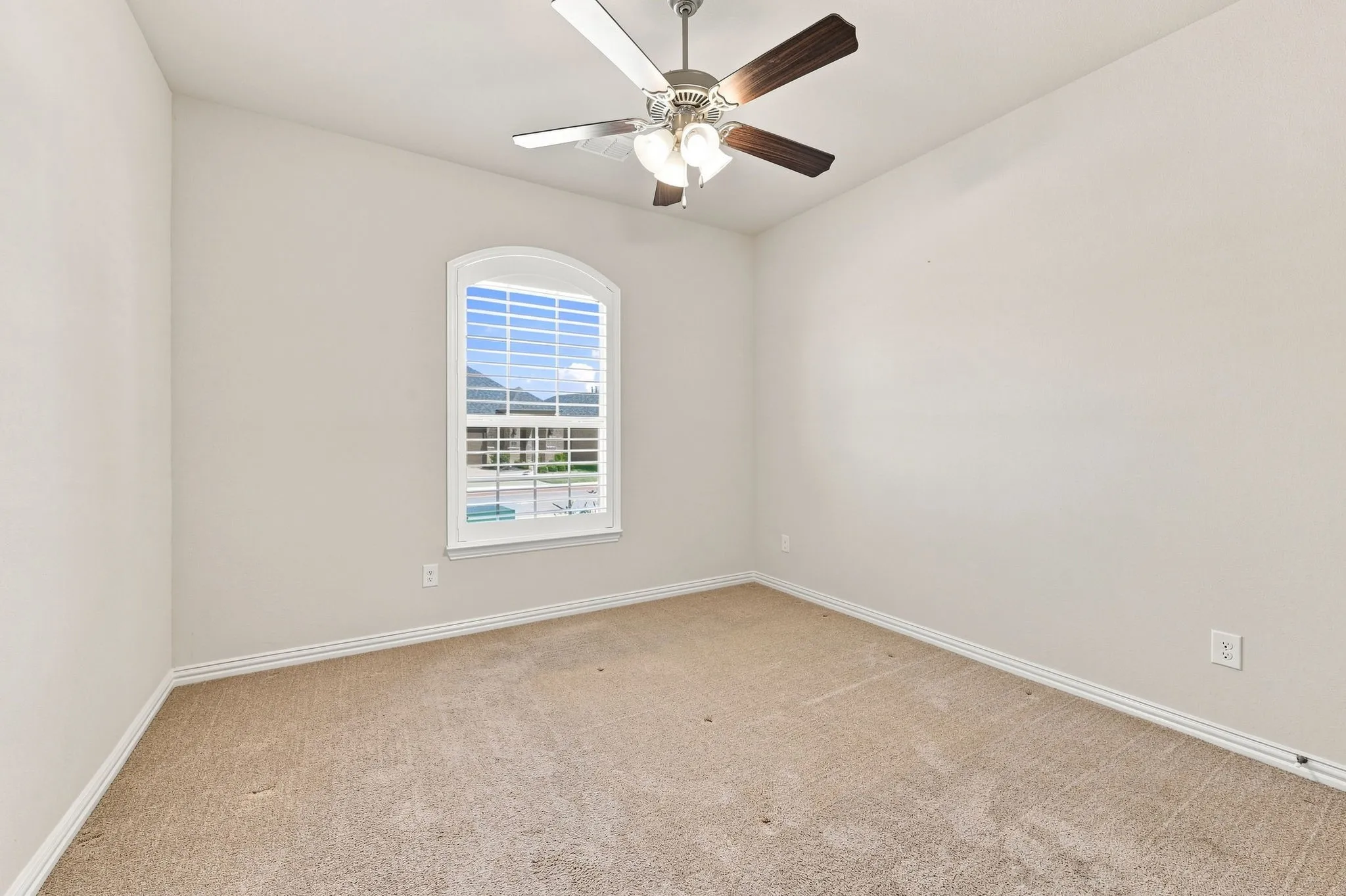 Arched window with blinds, ceiling fan with light fixture, and neutral carpet flooring