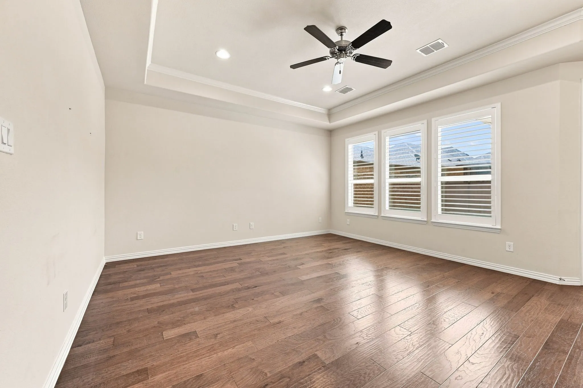Tray ceiling with recessed lighting, ceiling fan, wood-finish flooring, and multiple windows with blinds