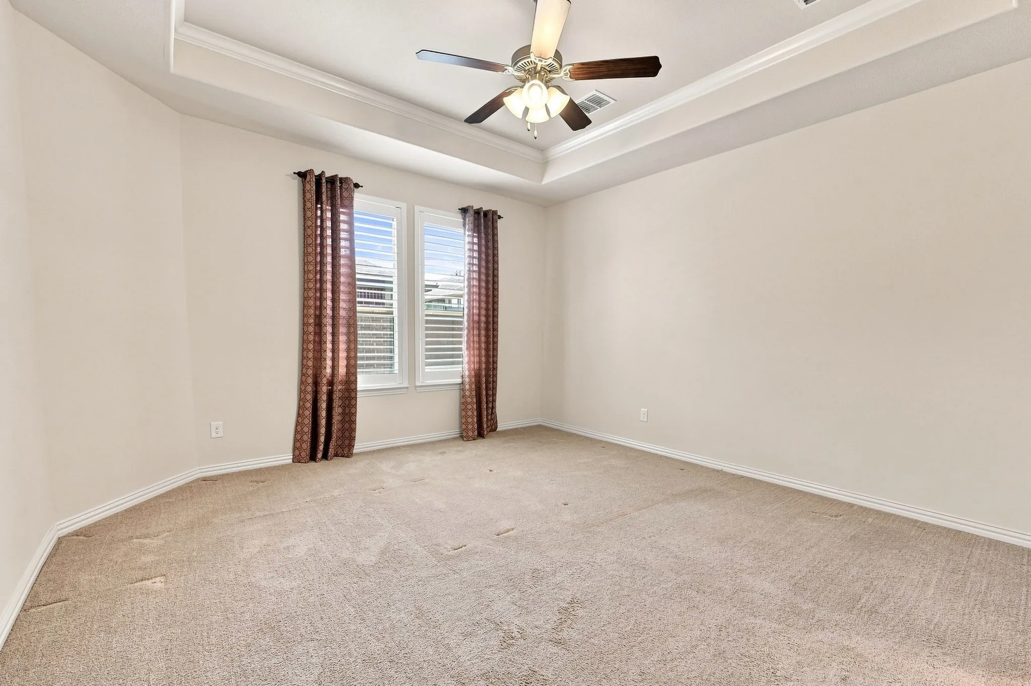 Tray ceiling with crown molding, ceiling fan, and two windows with plantation shutters