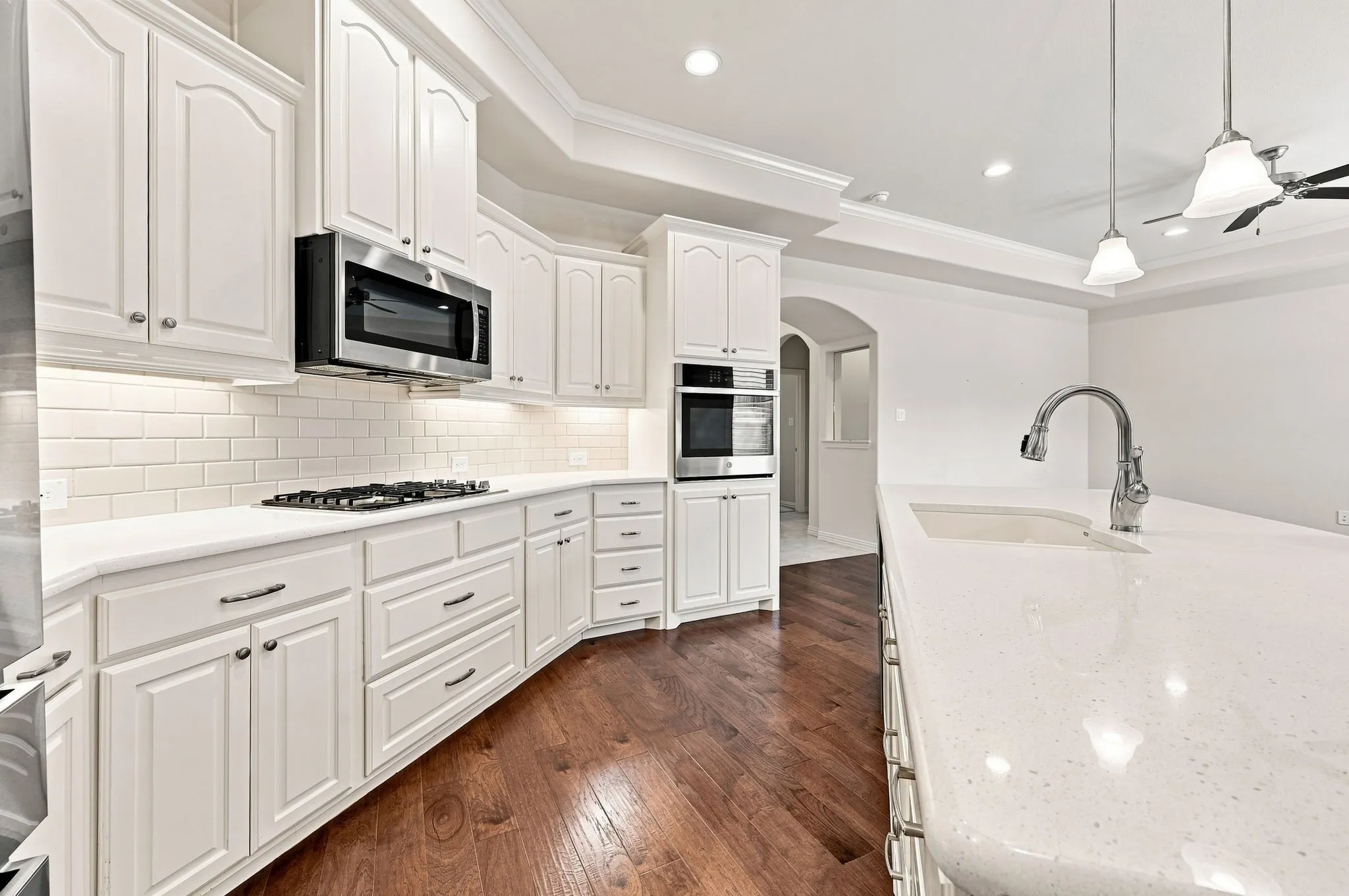 White shaker-style cabinetry with dark hardware, stainless steel appliances, subway tile backsplash, light-toned countertops, and wood-finish flooring