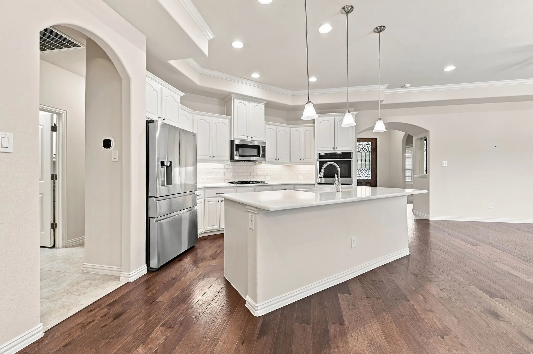 Kitchen featuring white cabinetry, stainless steel appliances, a center island with a sink, pendant lighting, and dark wood-finish flooring