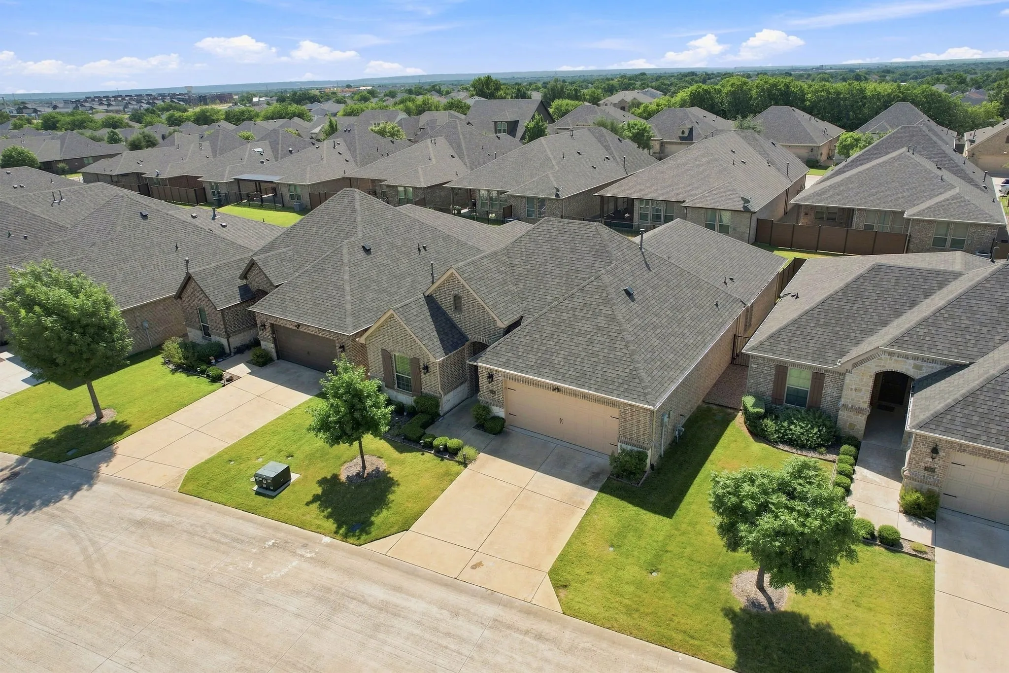 Aerial perspective of a residential street with multiple single-story homes, featuring concrete driveways and shingled roofs
