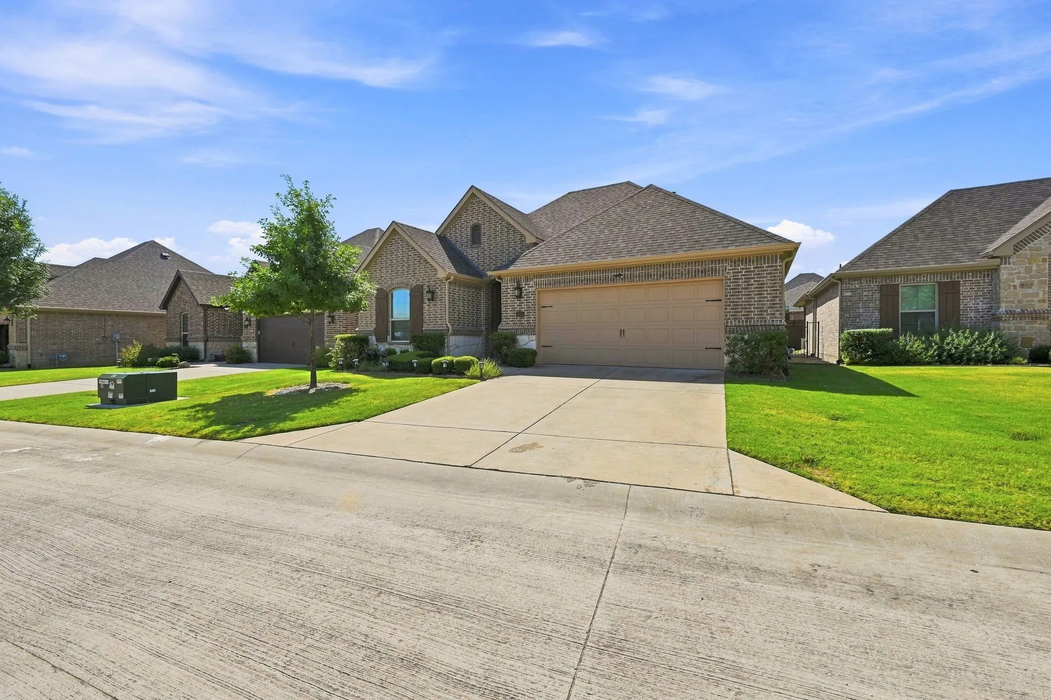 Brick exterior, two-car garage, concrete driveway, front yard landscaping, and gabled roofline