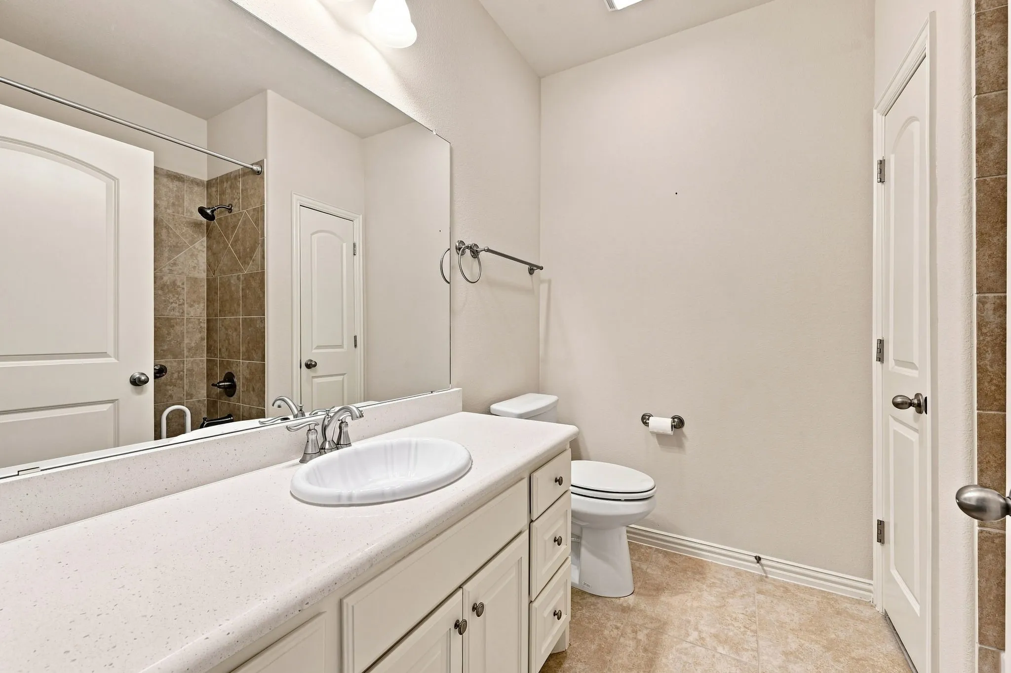 Spacious vanity with an integrated sink and chrome fixtures, ample built-in cabinet storage, a full-width mirror, and tiled shower surround