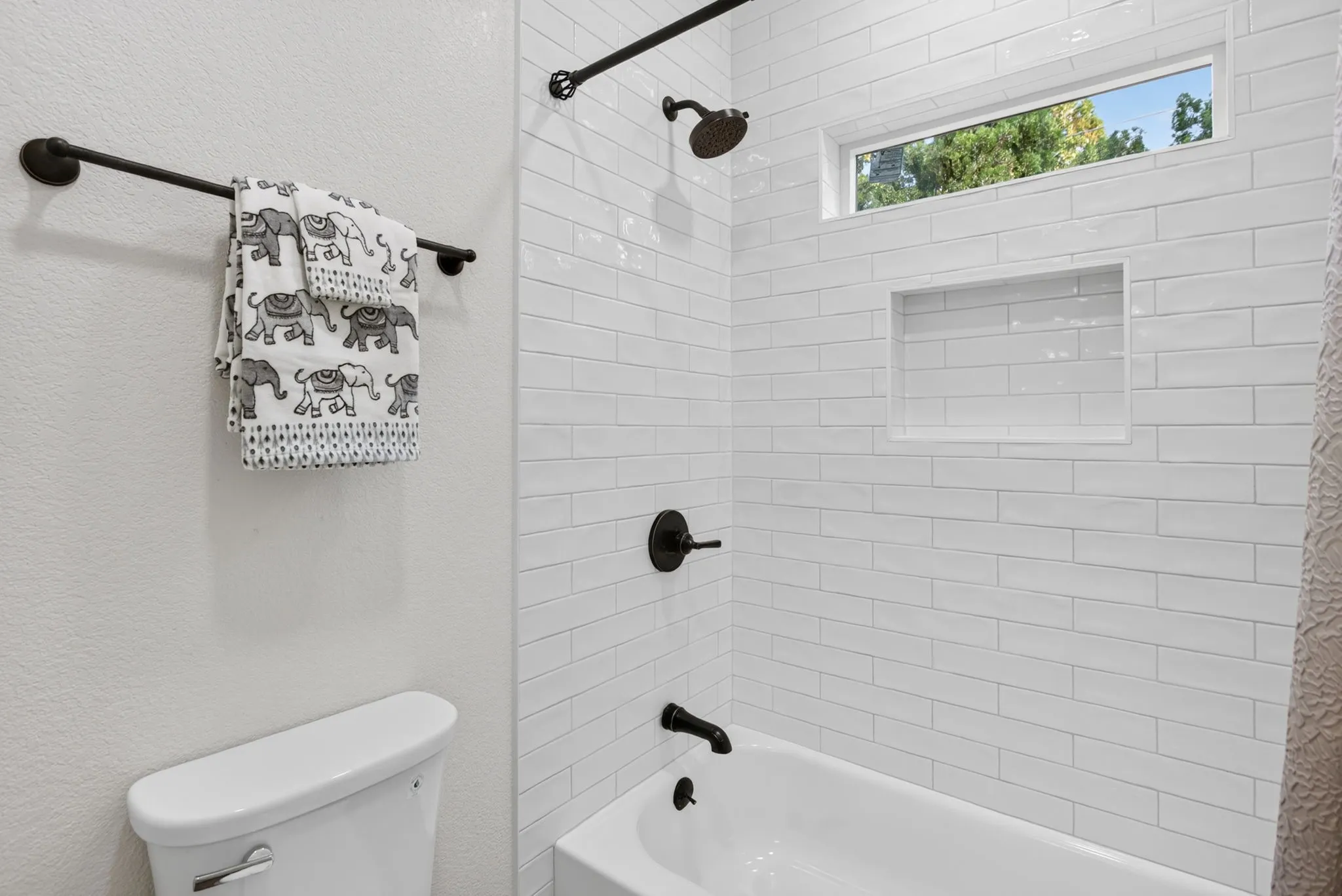 Freshly tiled tub-shower combo with product niche and transom window.