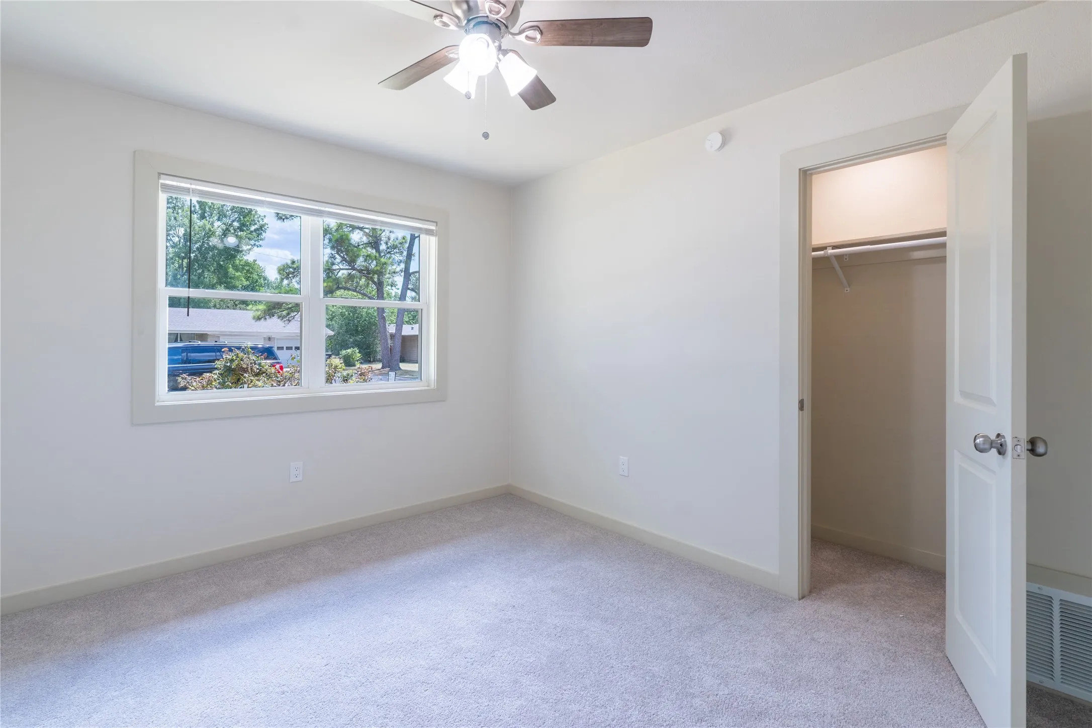 Window with white trim, ceiling fan, neutral carpet, and white door with brushed nickel hardware