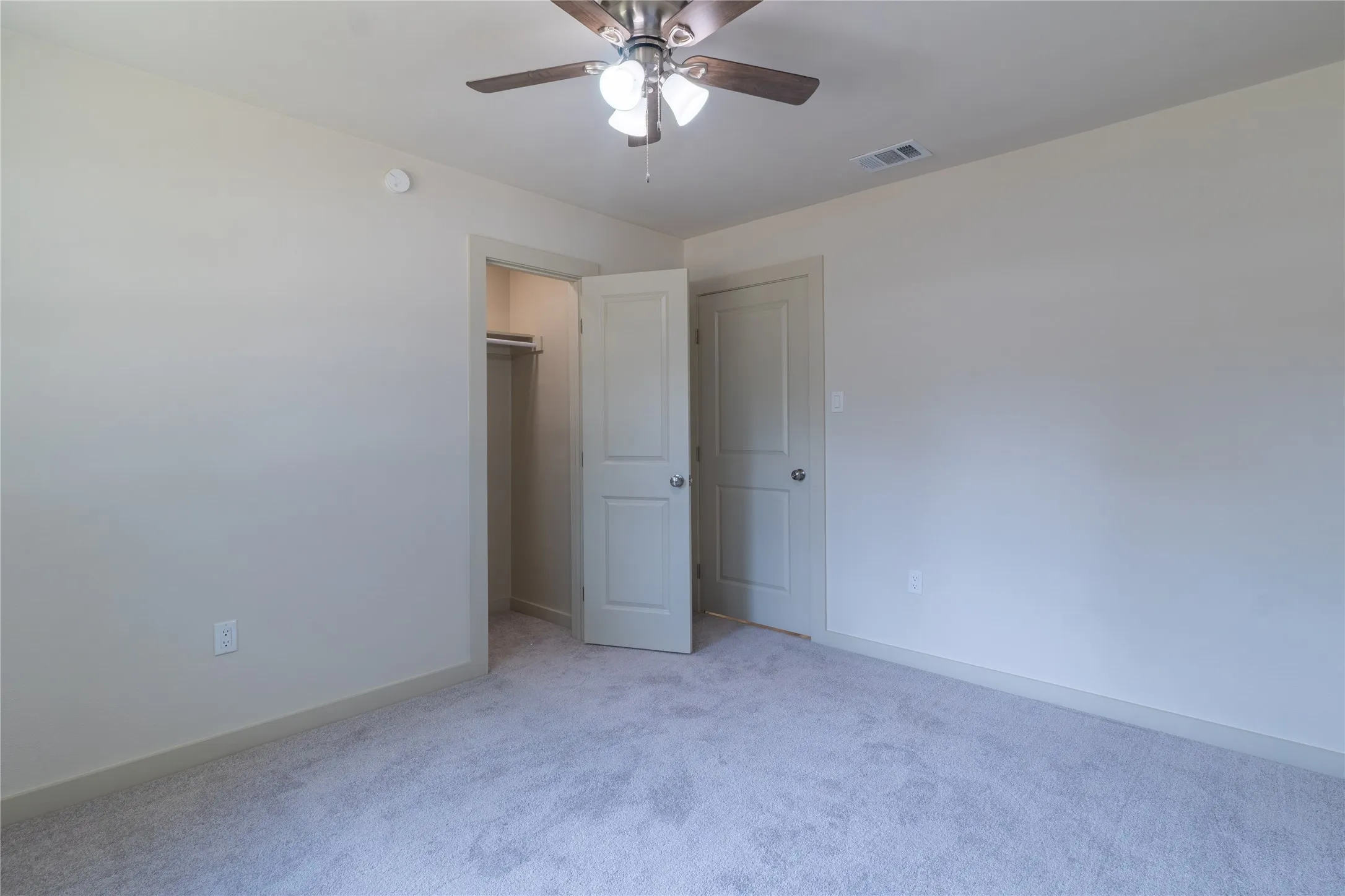 Carpeted flooring, neutral wall color, ceiling fan with integrated lighting, two panel interior doors, and a built-in closet with hanging rod