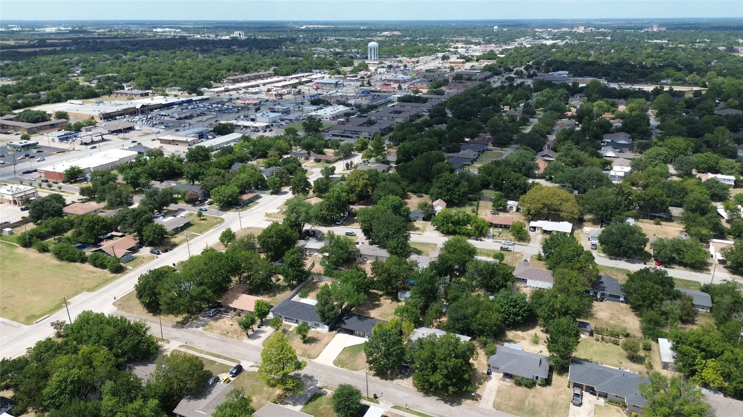 Aerial perspective featuring residential properties, mature trees, and commercial structures