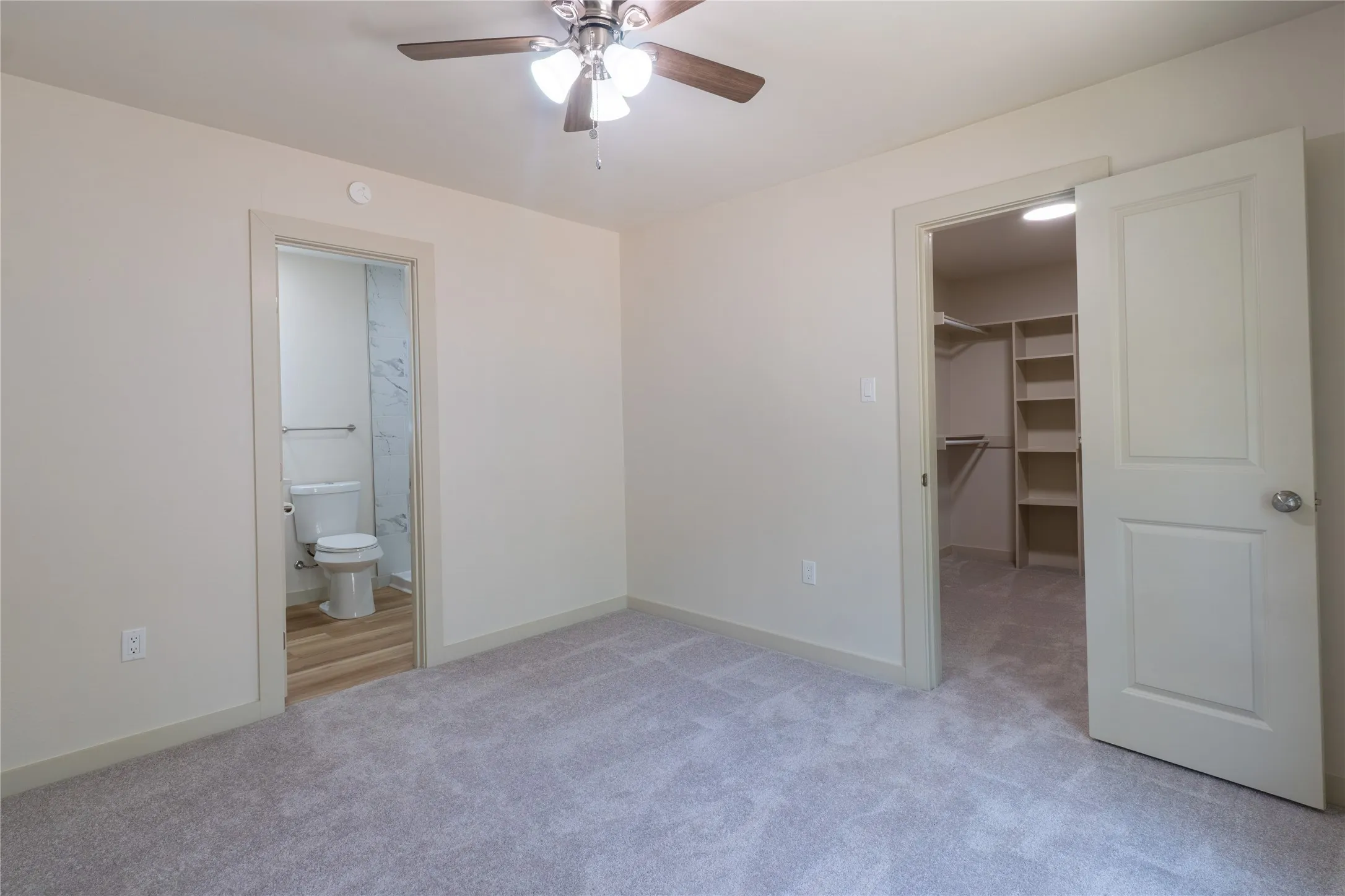 Plush carpeting, ceiling fan with integrated lighting, closet with built-in shelving, and an en-suite bathroom featuring wood-finish flooring and a toilet