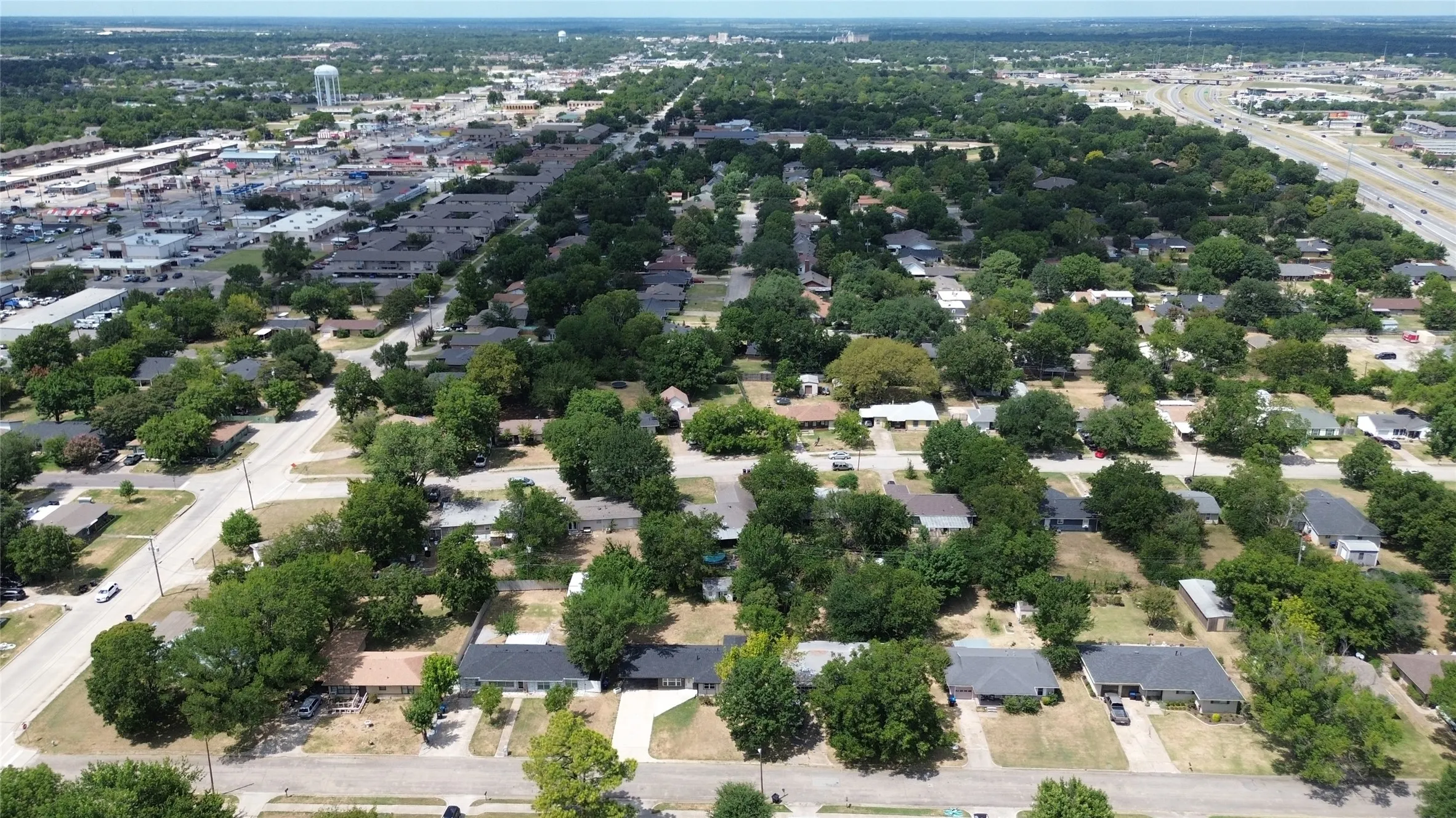 Aerial perspective showcasing residential properties with established trees, paved streets, and commercial areas in the background