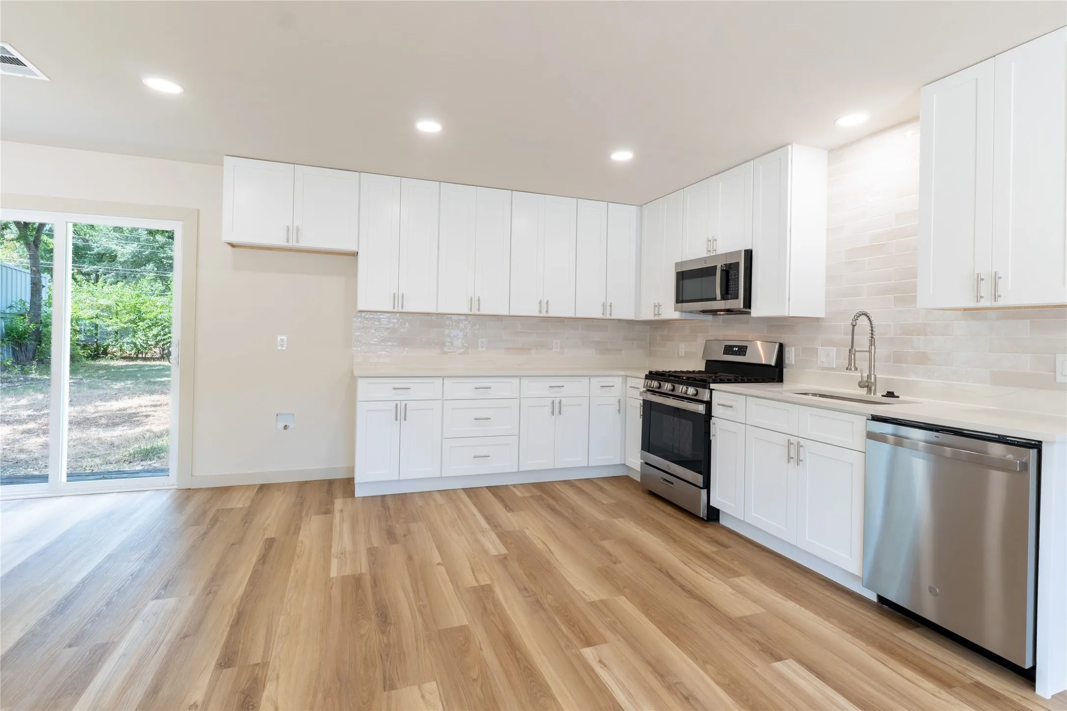 Kitchen featuring wood-finish flooring, white cabinetry, stainless steel appliances, light-toned countertops, and a full-height tile backsplash
