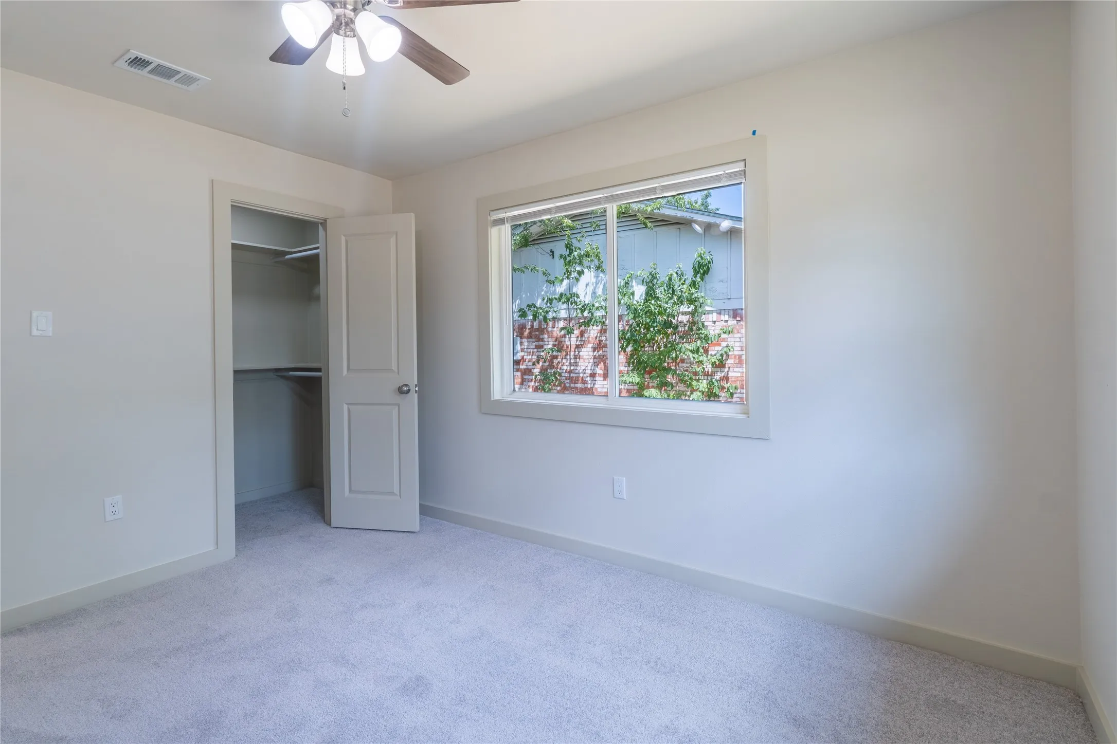 Neutral carpet flooring, ceiling fan with integrated lighting, and a window providing natural light