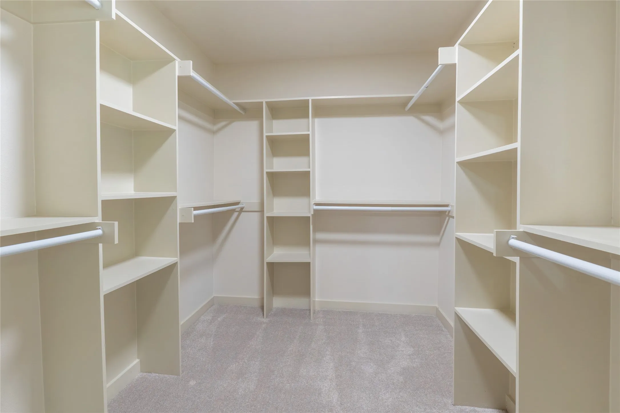 Expansive closet featuring integrated shelving, multiple hanging rods, and light-toned carpeting
