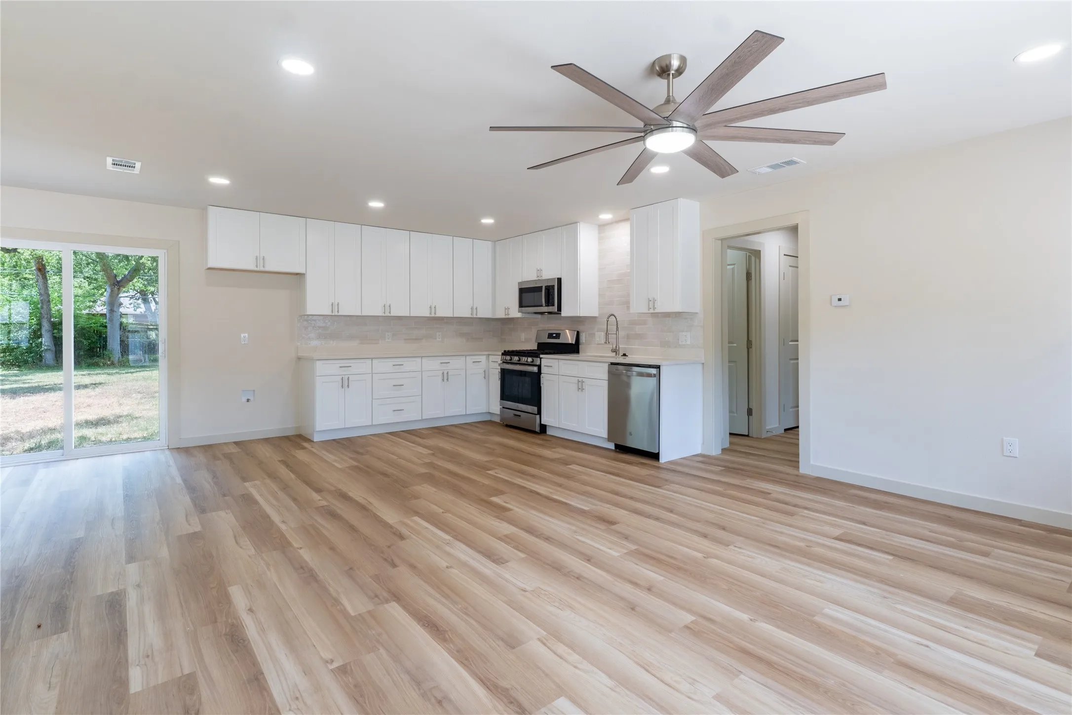 Spacious open-concept living area with wood-finish flooring, recessed lighting, and a modern ceiling fan