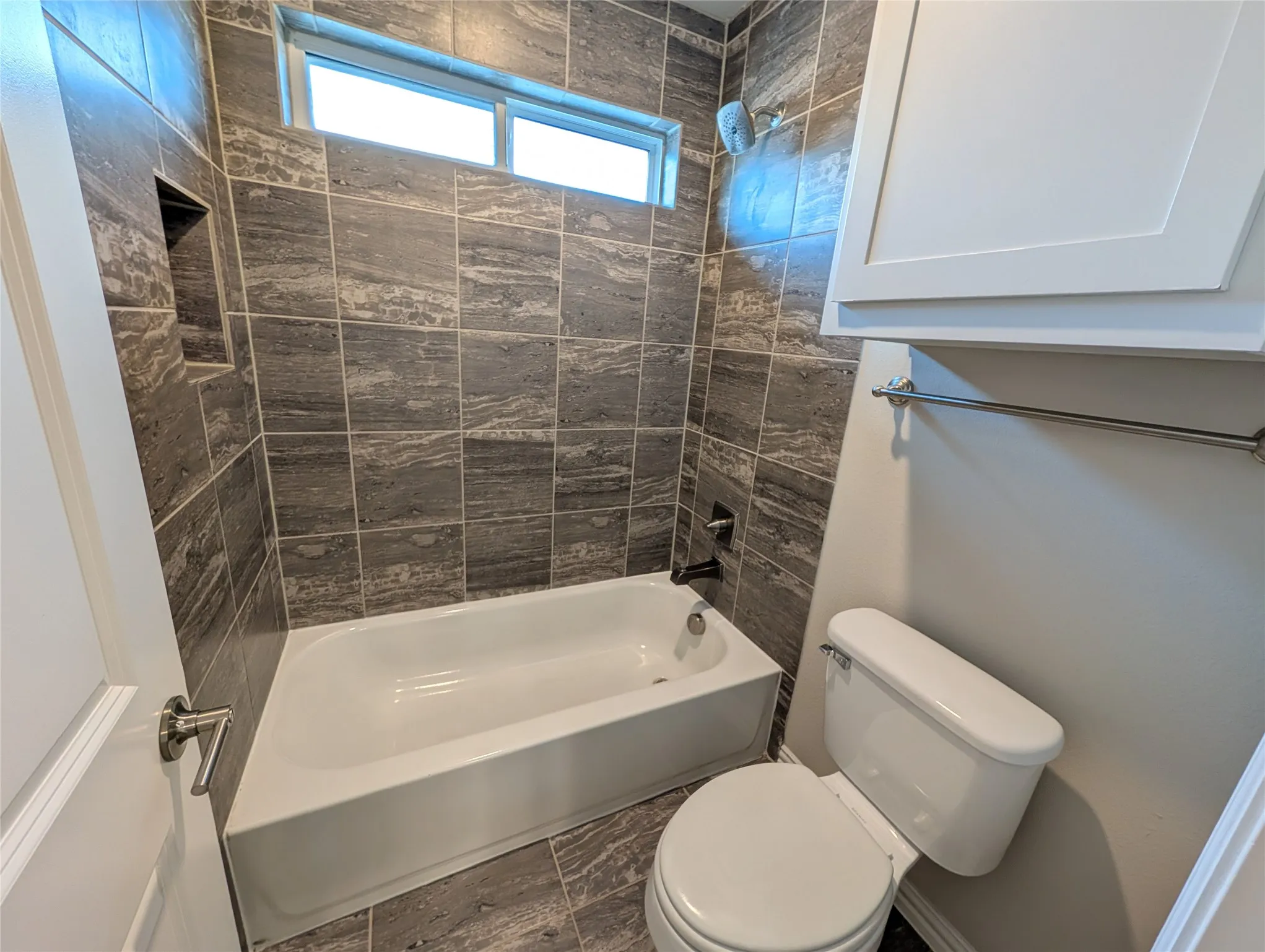 White bathtub featuring a dark bronze faucet, integrated shower niche, and a horizontal window