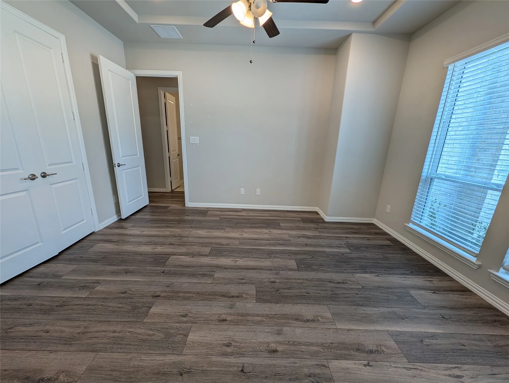 Tray ceiling with recessed lighting, ceiling fan, wood-finish flooring, and multiple windows with blinds