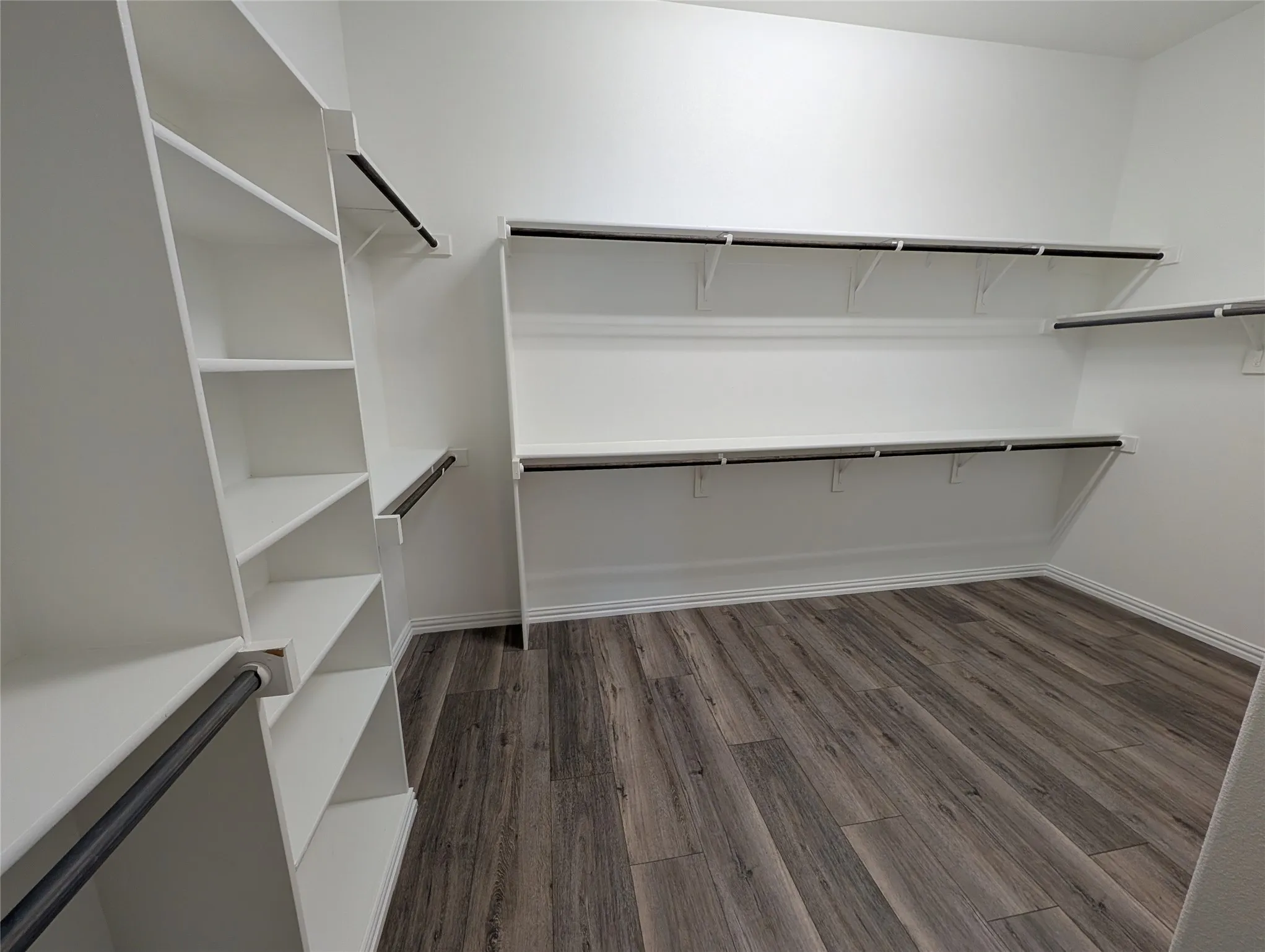 Expansive walk-in closet featuring wood-finish flooring, white walls, built-in shelving, and multiple hanging rods