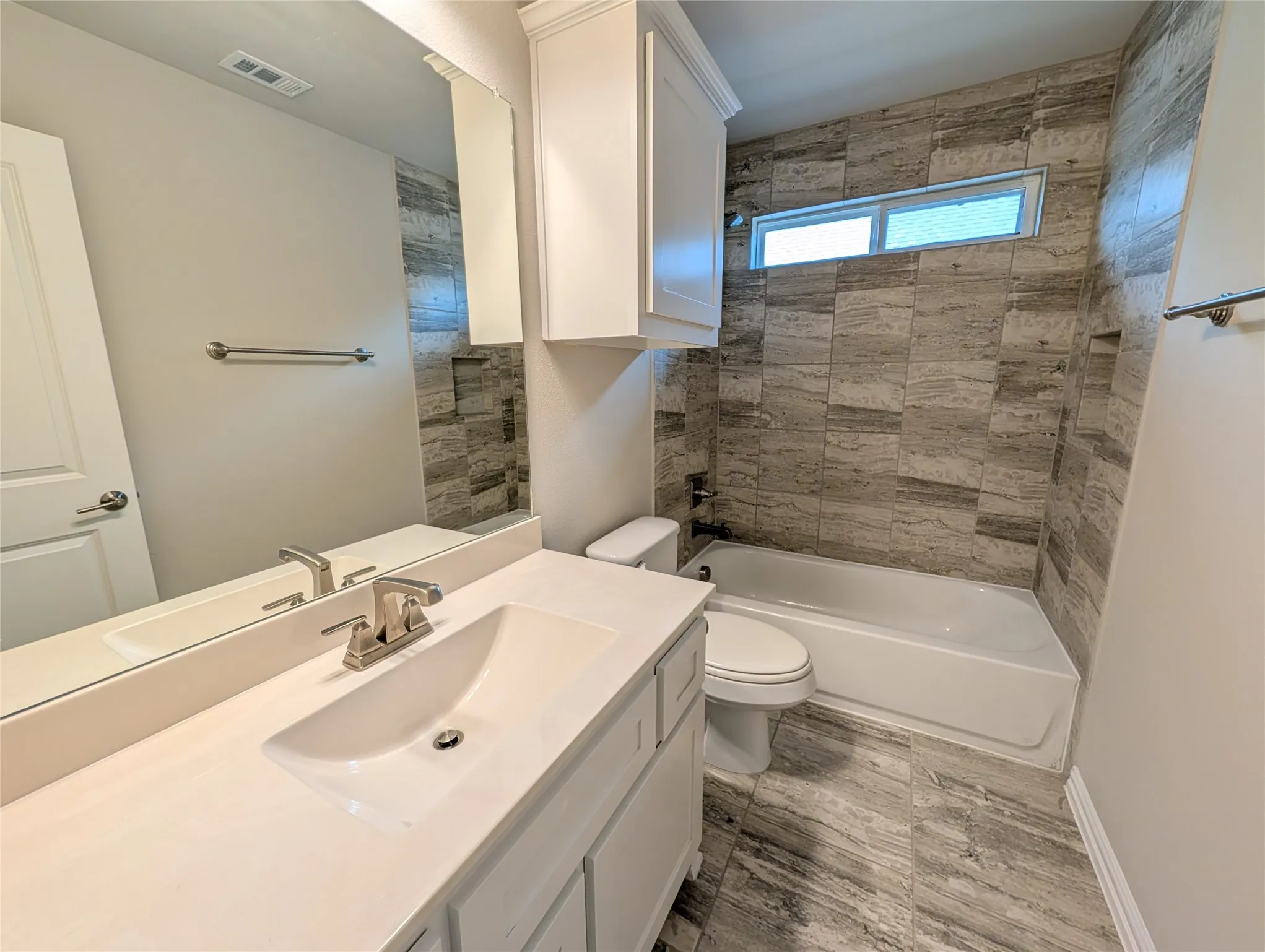 White vanity with an integrated sink, brushed nickel faucet, large wall mirror, and overhead white cabinetry