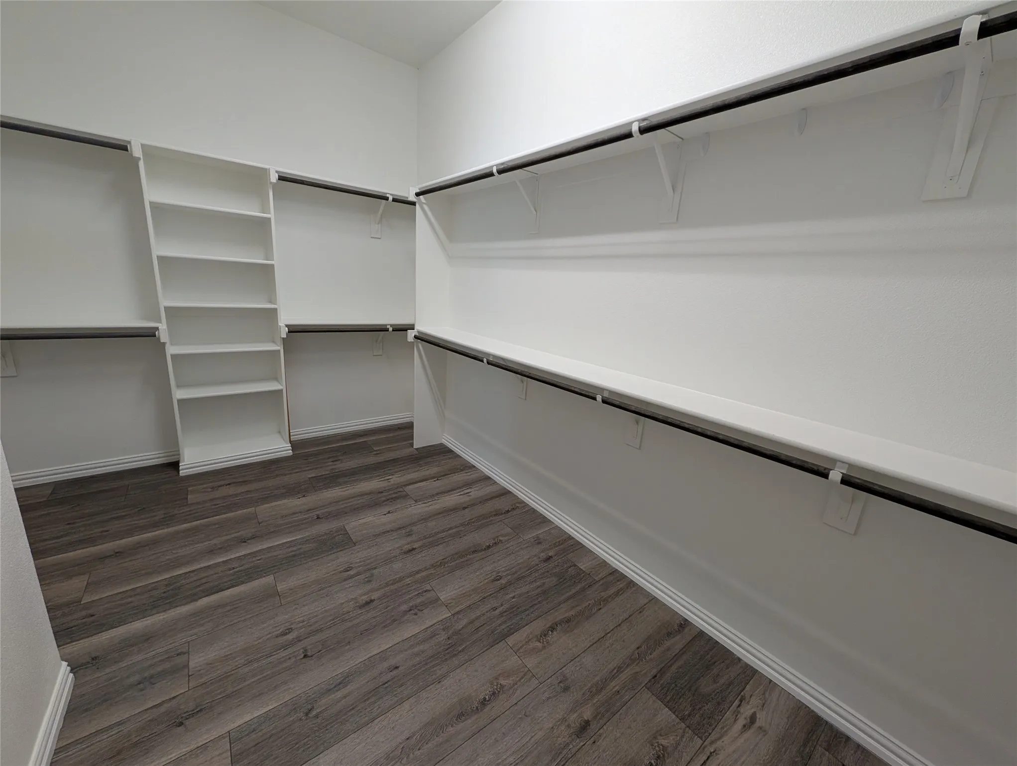 Expansive walk-in closet featuring wood-finish flooring, built-in shelving, and multiple clothing rods