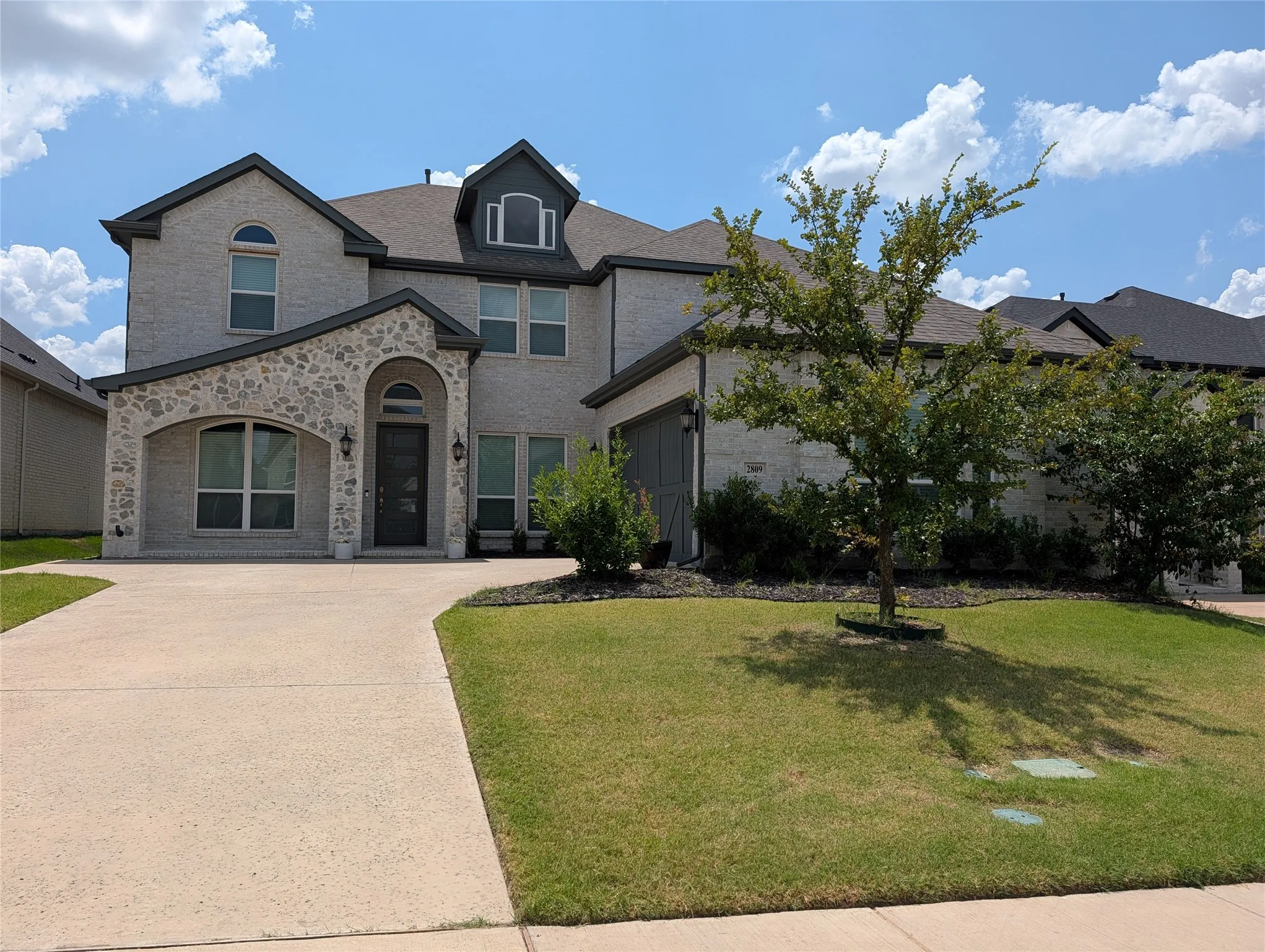 Two-story residence featuring light-toned brick and stone veneer, an arched entry, a dark-toned front door, and a two-car garage with a complementary dark-toned door