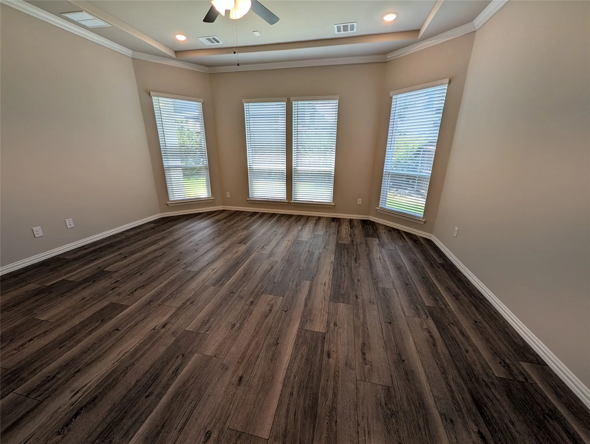 Wood-finish flooring, multiple windows with blinds, tray ceiling with crown molding, recessed lighting, and a ceiling fan