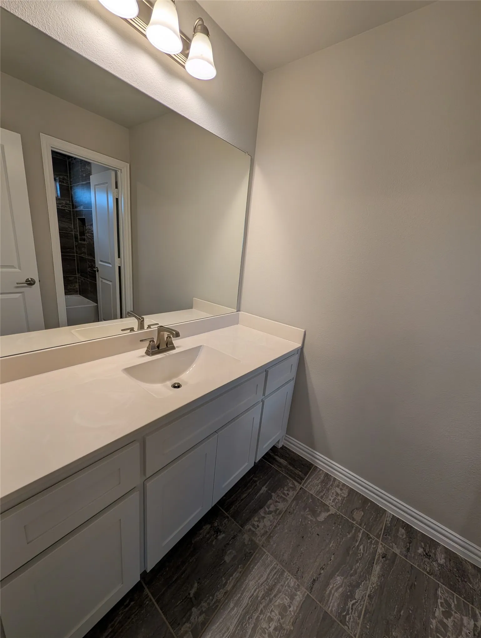 Vanity with an integrated sink, brushed nickel faucet, large wall mirror, three-light vanity fixture, and tiled flooring