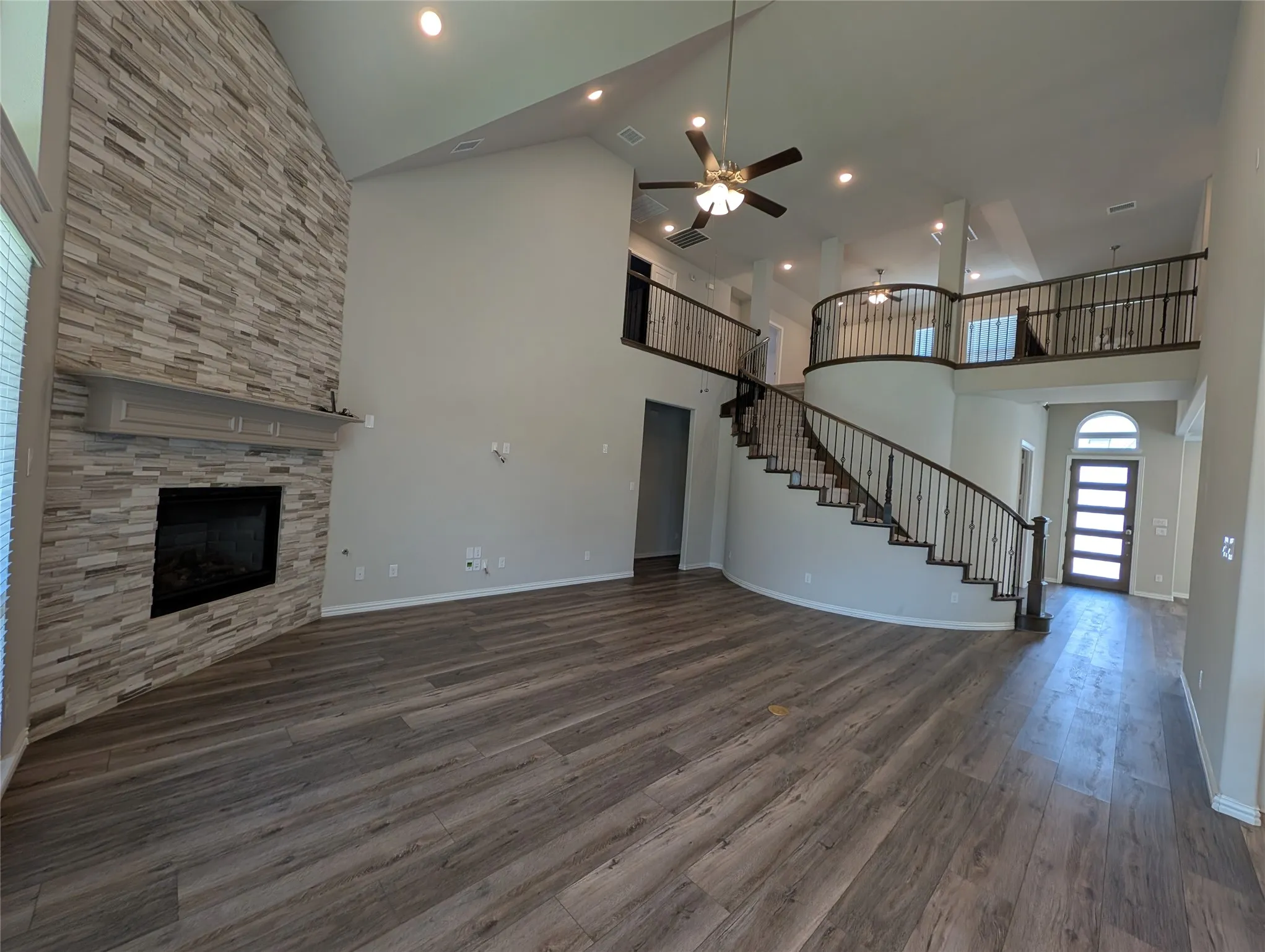 Two-story living area with a stone-clad fireplace, wood-finish flooring, and a curved staircase with wrought iron balusters