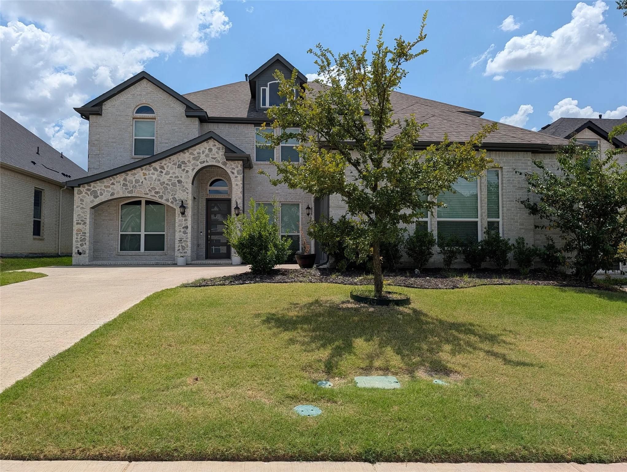 Exterior featuring light-colored brick with stone accents, a multi-gabled roofline, an arched entry, and a prominent front-facing window