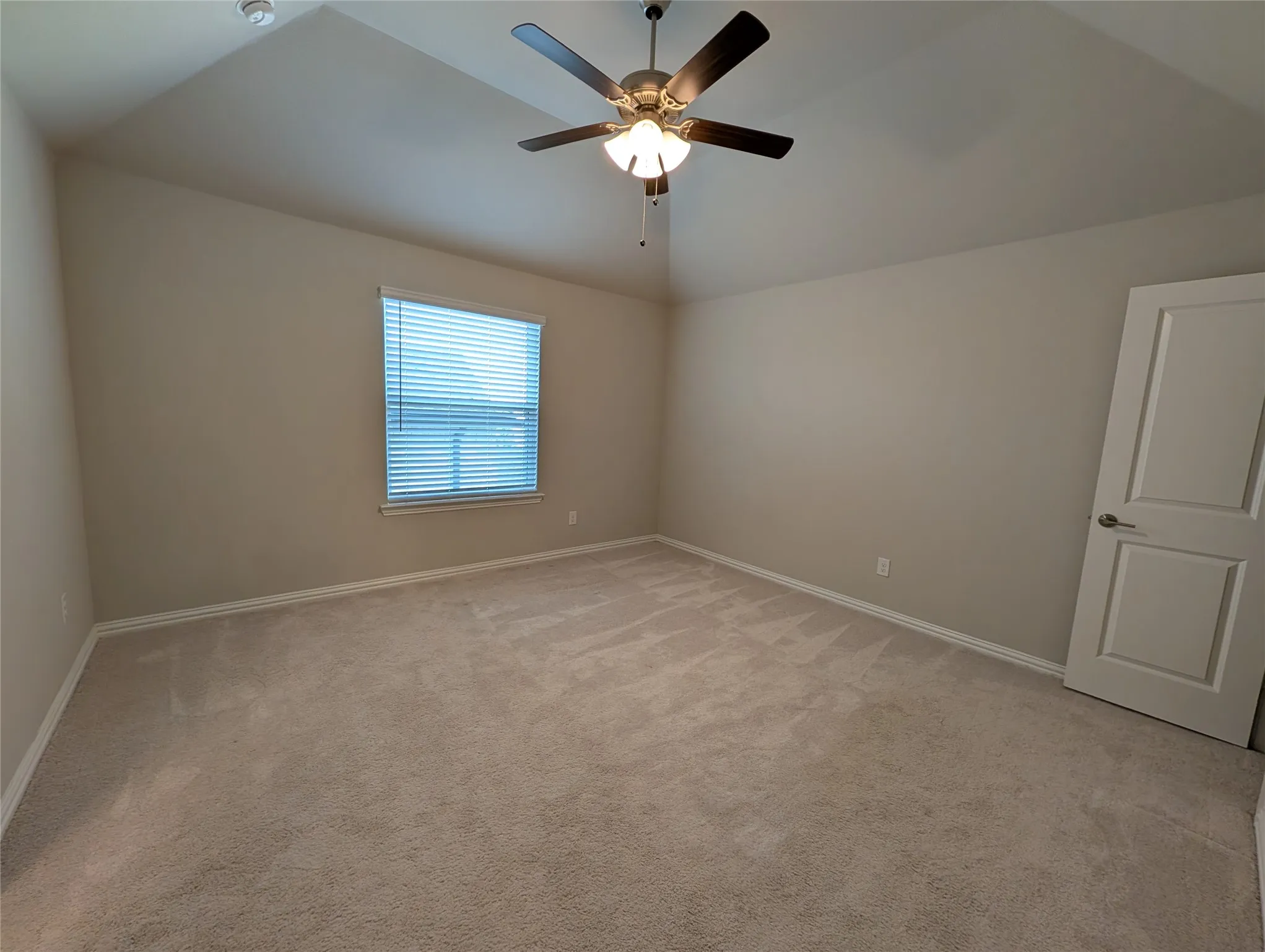 Vaulted ceiling with an integrated ceiling fan and light fixture, light-colored carpeting, and a window with blinds
