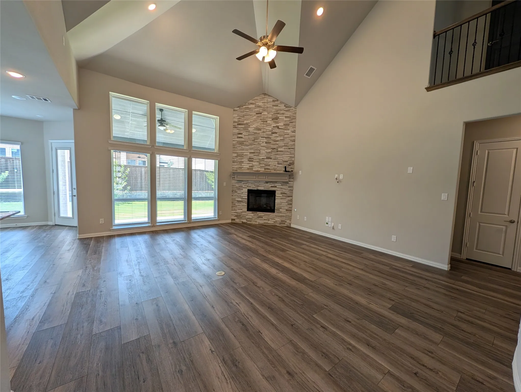 Soaring vaulted ceilings with recessed lighting, floor-to-ceiling windows, wood-finish flooring, and a stone-clad fireplace with a wood mantel