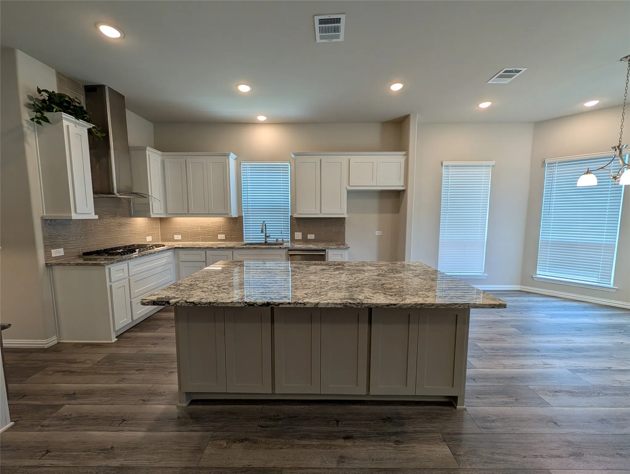 Kitchen featuring an expansive island, granite countertops, wood-finish flooring, a tile backsplash, and recessed lighting
