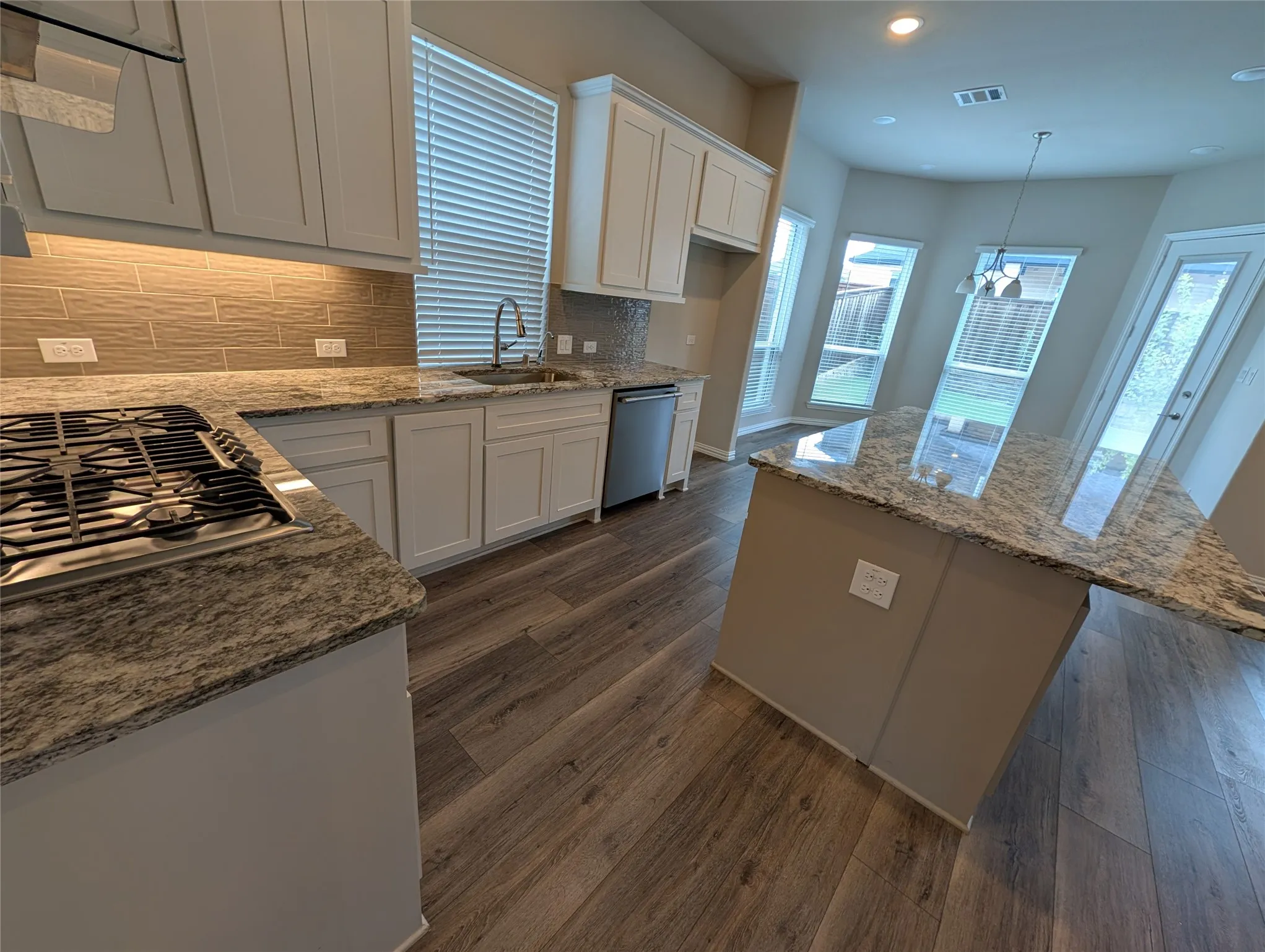 Kitchen featuring wood-finish flooring, white cabinetry, granite countertops, a gas range, and a kitchen island with pendant lighting