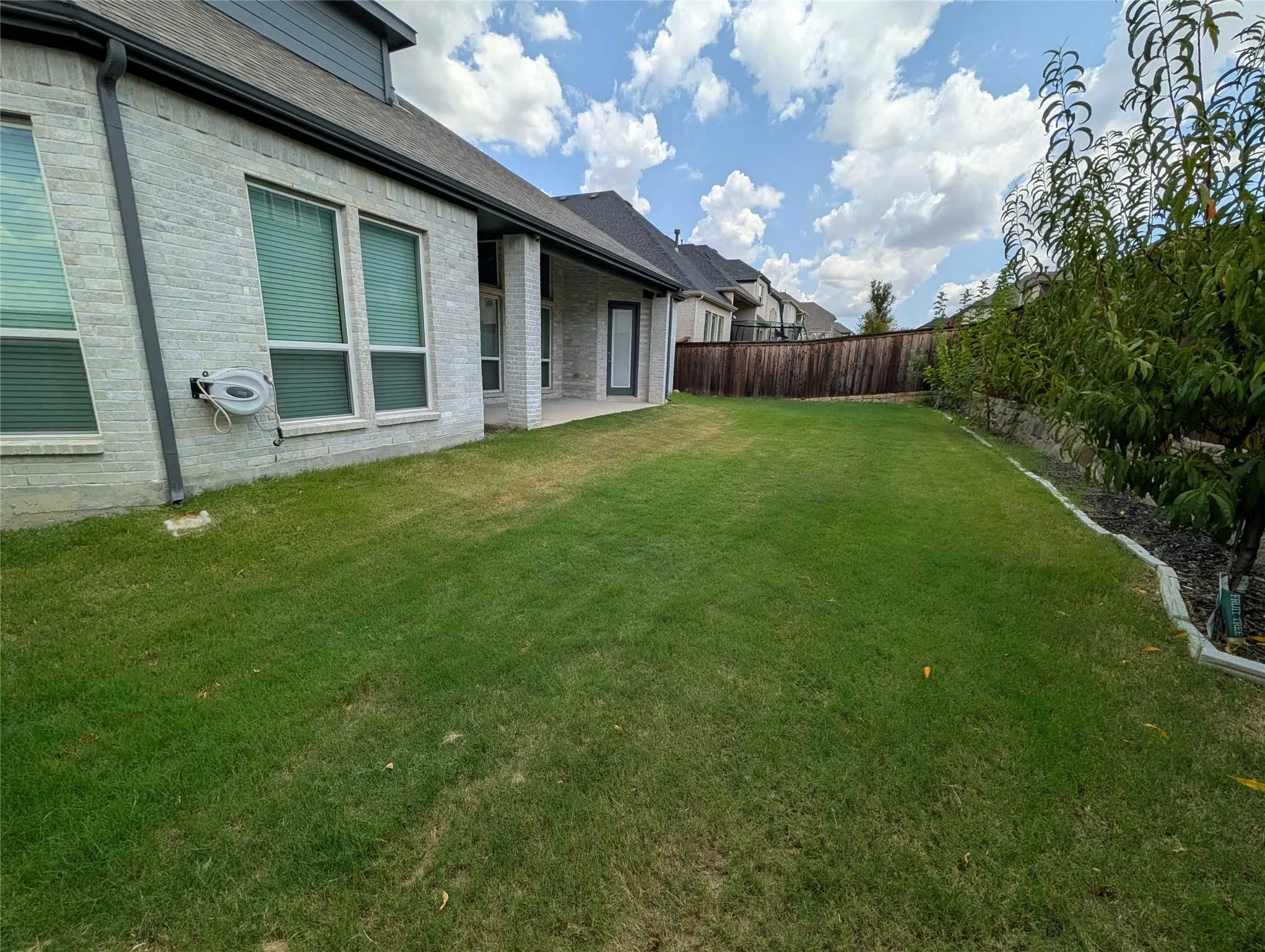 Expansive backyard featuring a manicured lawn, established privacy fencing, and a covered patio area