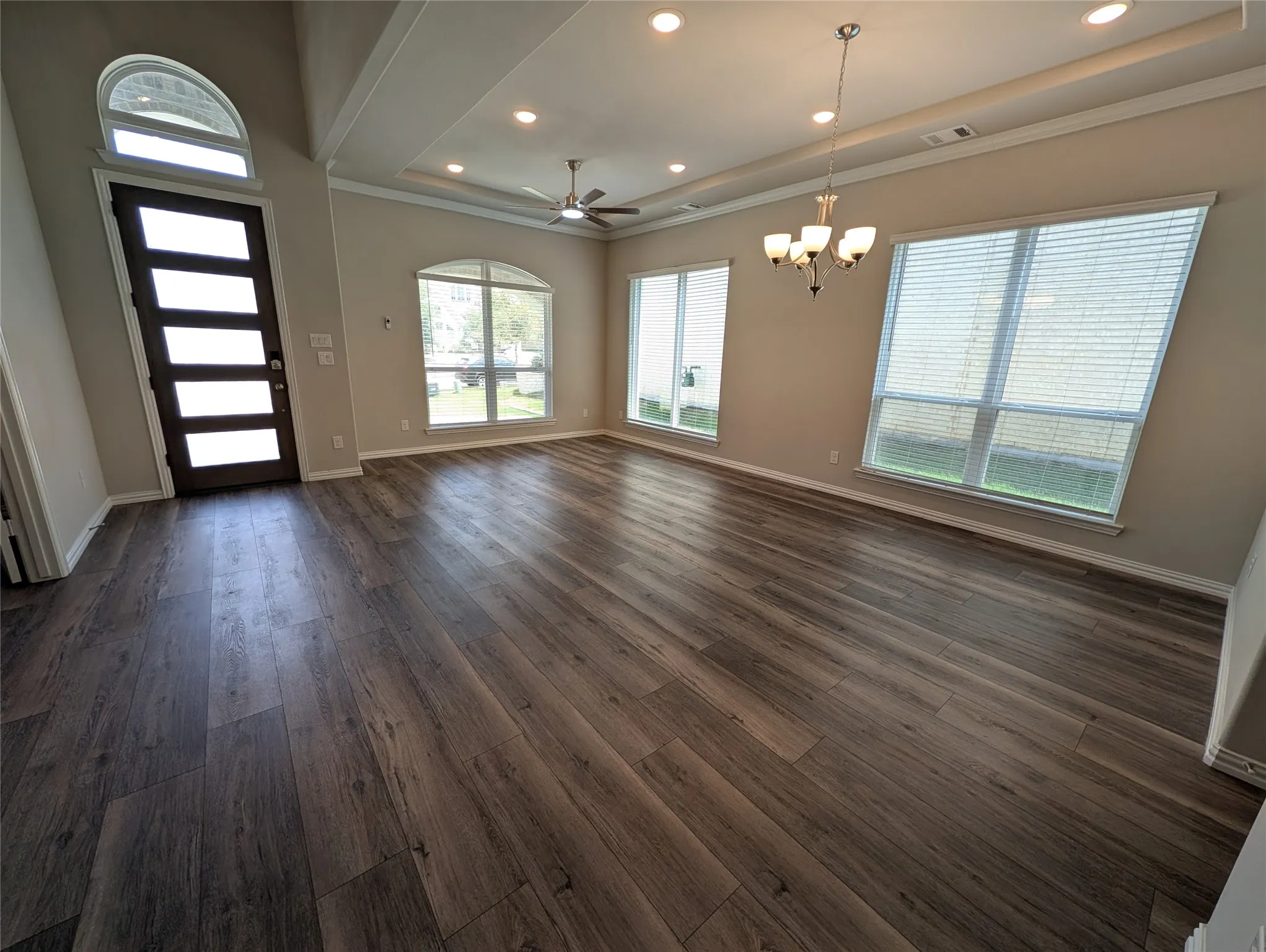 Wood-finish flooring throughout, tray ceiling with recessed lighting, modern chandelier, ceiling fan, and arched transom window above the entry door