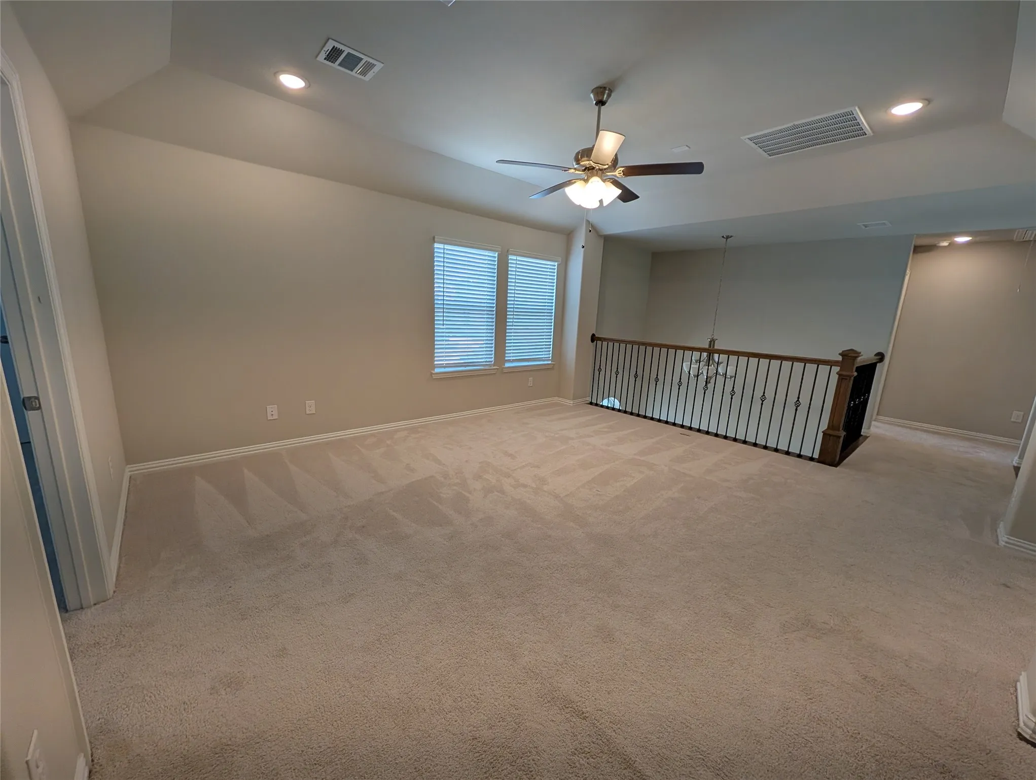 Carpeted area featuring a ceiling fan, recessed lighting, and a wrought iron and wood banister