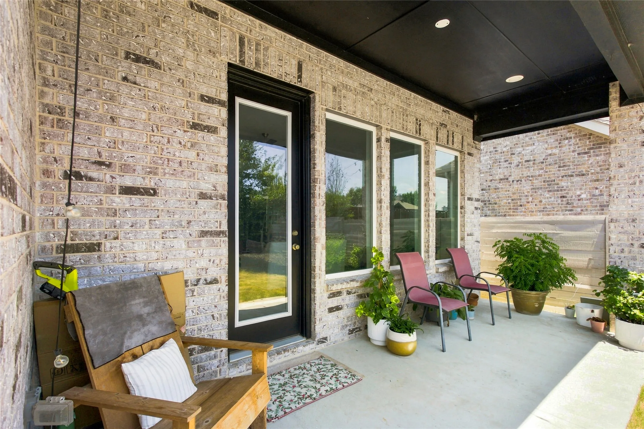 Covered patio featuring a solid brick exterior, a black overhead ceiling with recessed lighting, a full-light entry door, and multiple vertical windows