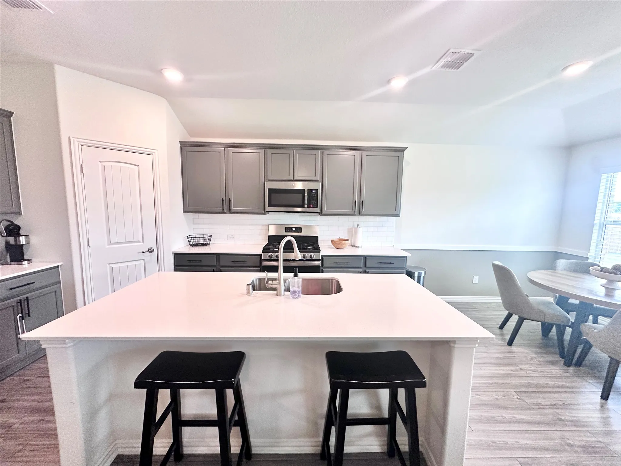 Beautifully appointed kitchen featuring a center island with an undermount sink, sleek gray cabinetry, stainless steel appliances, wood-look flooring, and an adjoining breakfast area perfect for casual dining.