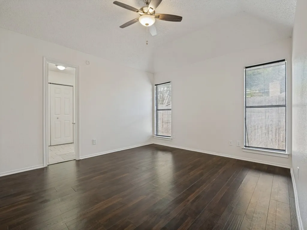 Primary- Vaulted ceiling featuring a ceiling fan with integrated lighting, wood-finish flooring, and multiple windows with horizontal blinds