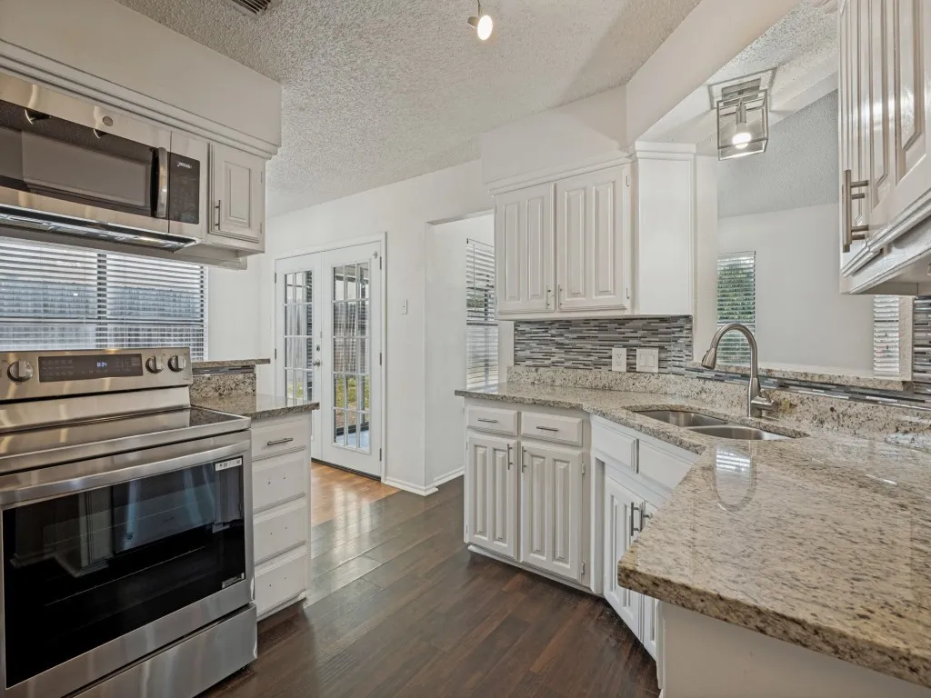 White cabinetry with brushed nickel hardware, light-toned granite countertops, and a mosaic tile backsplash