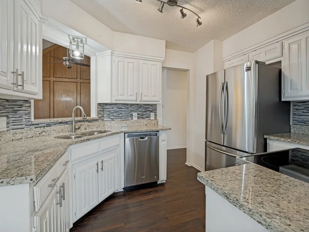 White cabinetry with brushed nickel hardware, granite countertops, tile backsplash, stainless steel appliances, and dark wood-finish flooring