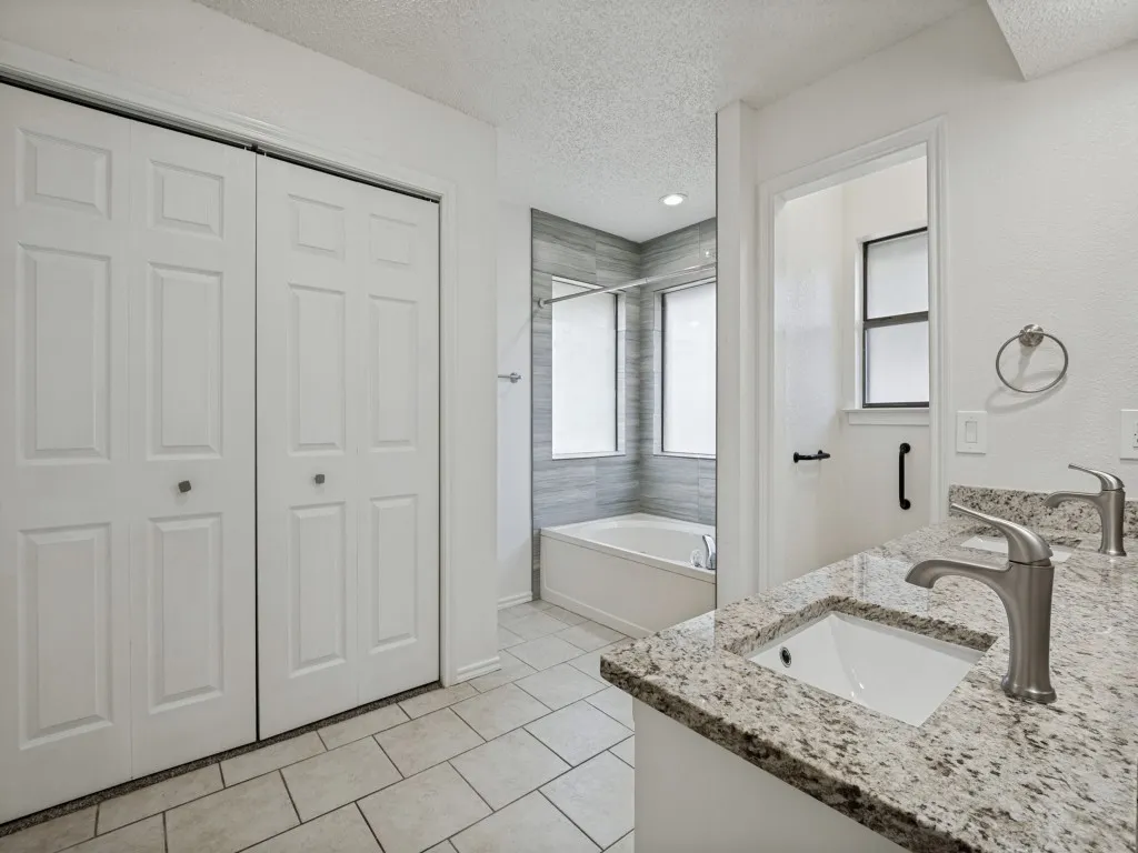 Primary Dual vanities with granite countertops, tile flooring, a built-in bathtub, and a tiled shower surround